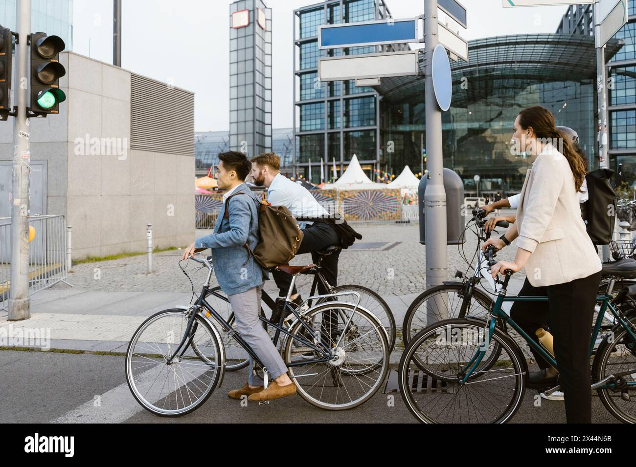 Männliche und weibliche Geschäftskollegen mit Fahrrädern, die an der Ampel warten, während sie zum Büro in der Stadt pendeln Stockfoto