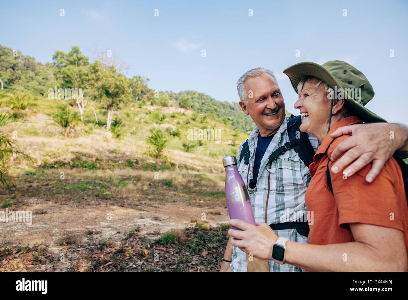 Lächelnder Seniorenmann mit Arm um Frau, die im Urlaub eine Wasserflasche hält Stockfoto