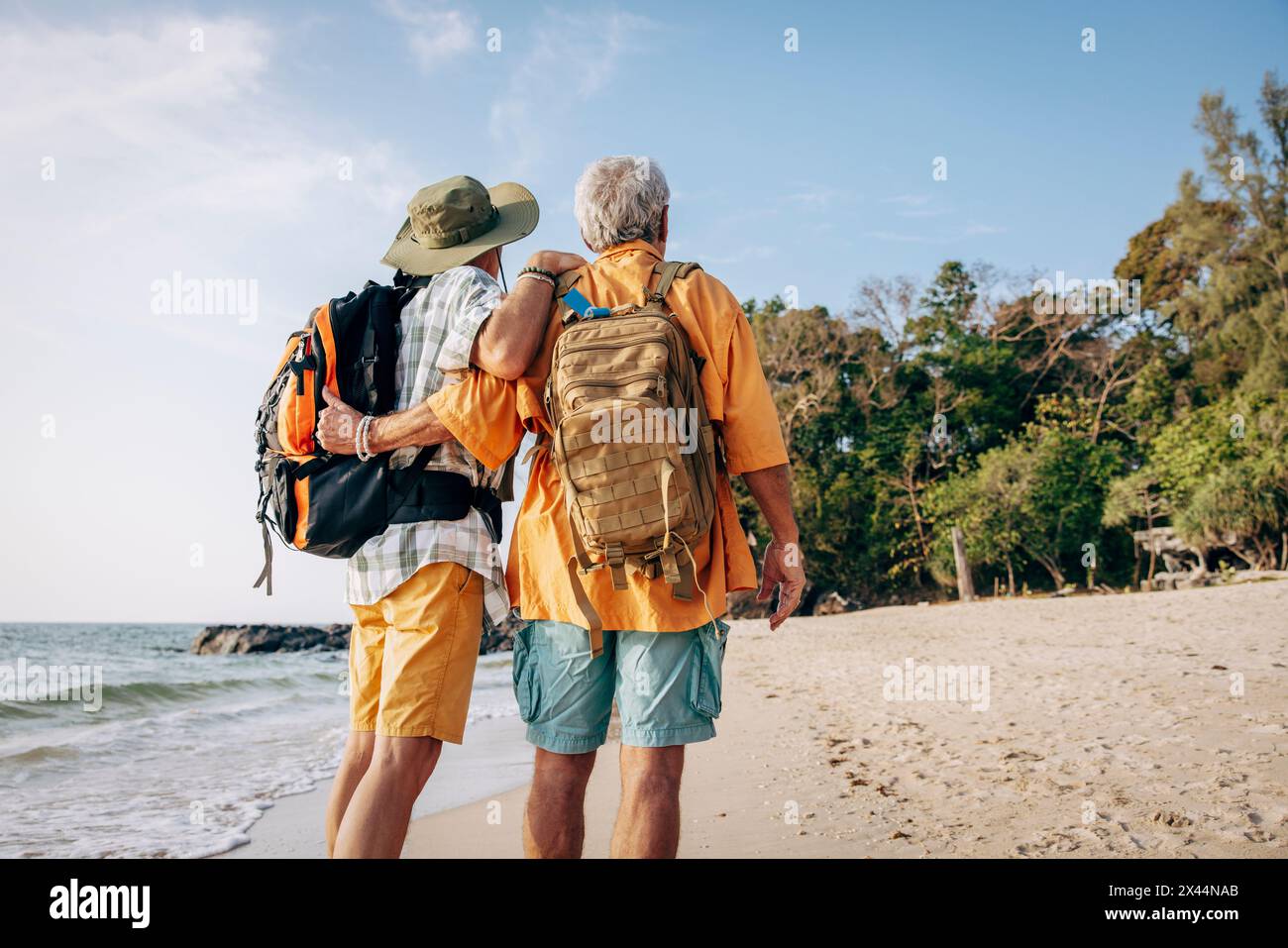 Flacher Rückblick auf ältere schwule Paare mit Rucksäcken, die im Urlaub am Strand stehen Stockfoto