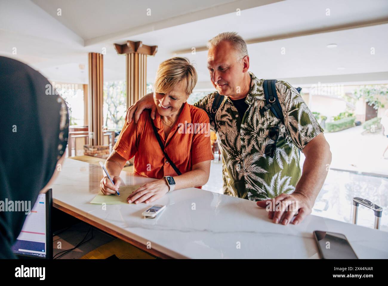 Lächelnde Seniorin, die das Formular mit einem Mann ausfüllt, während sie an der Rezeption im Hotel steht Stockfoto