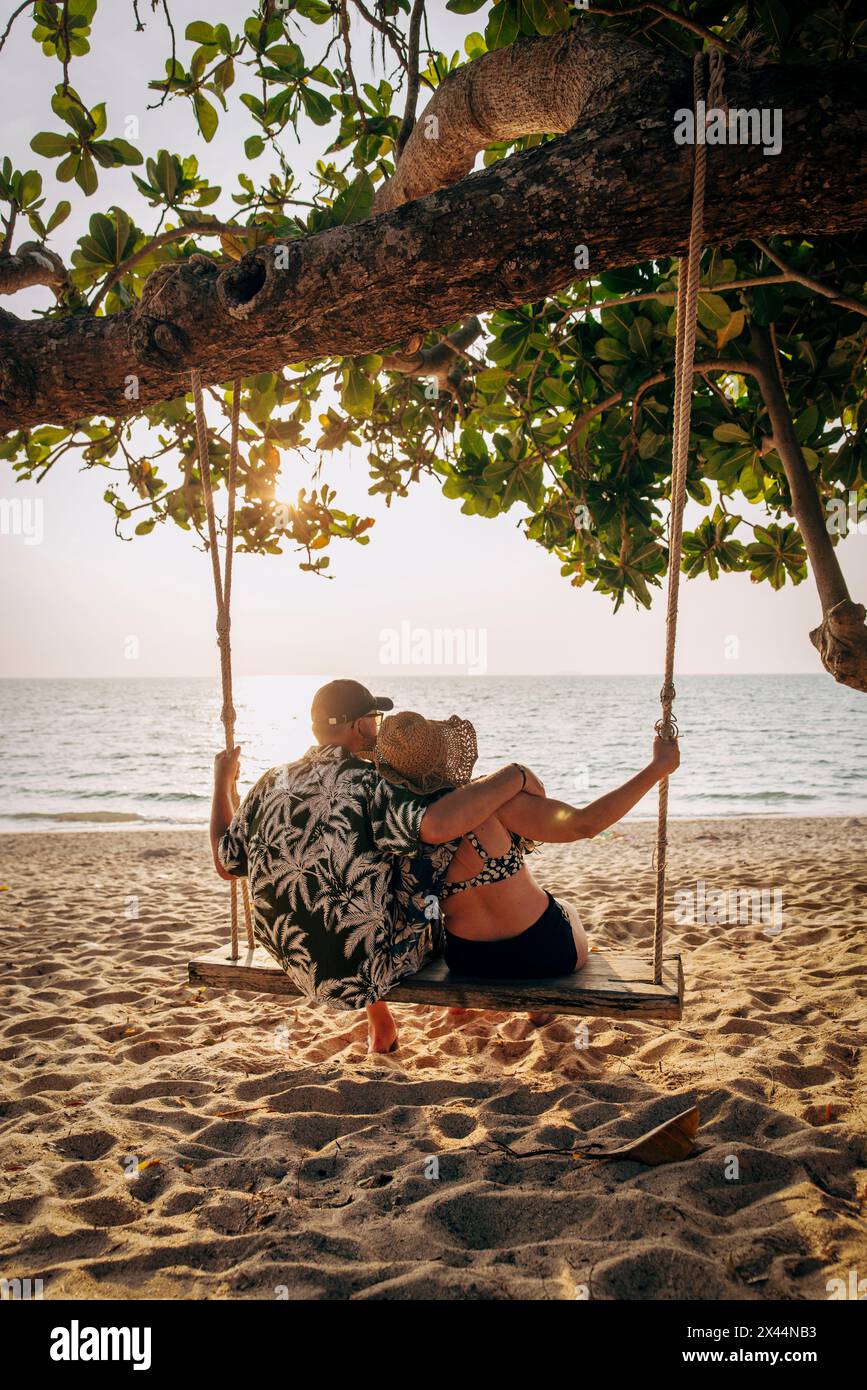Rückansicht eines romantischen Seniorenpaares, das auf der Schaukel sitzt und auf das Meer blickt Stockfoto