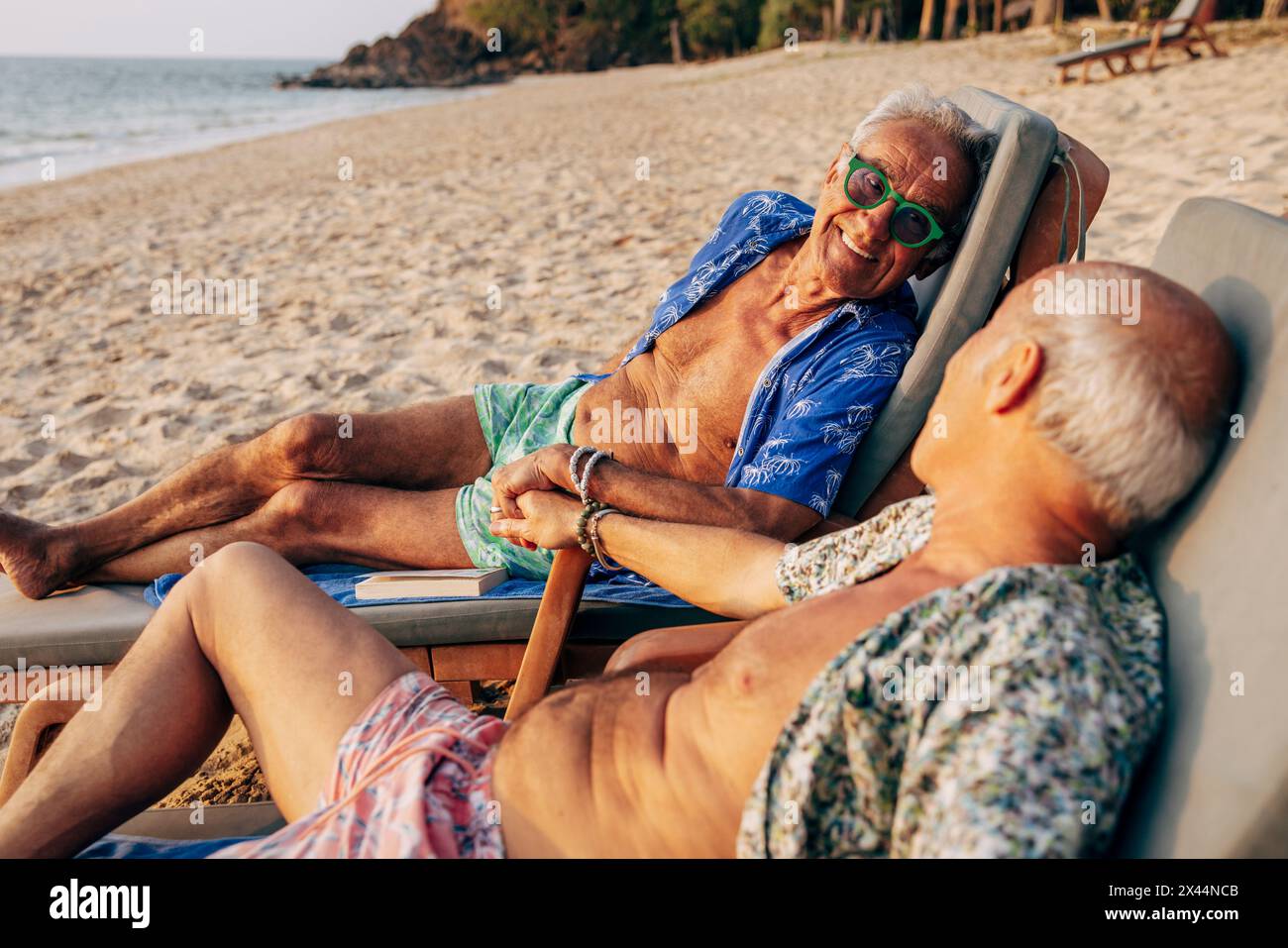 Ein lächelnder schwuler Mann verbrachte Urlaub mit einem Freund, der am Strand auf der Liege lag Stockfoto