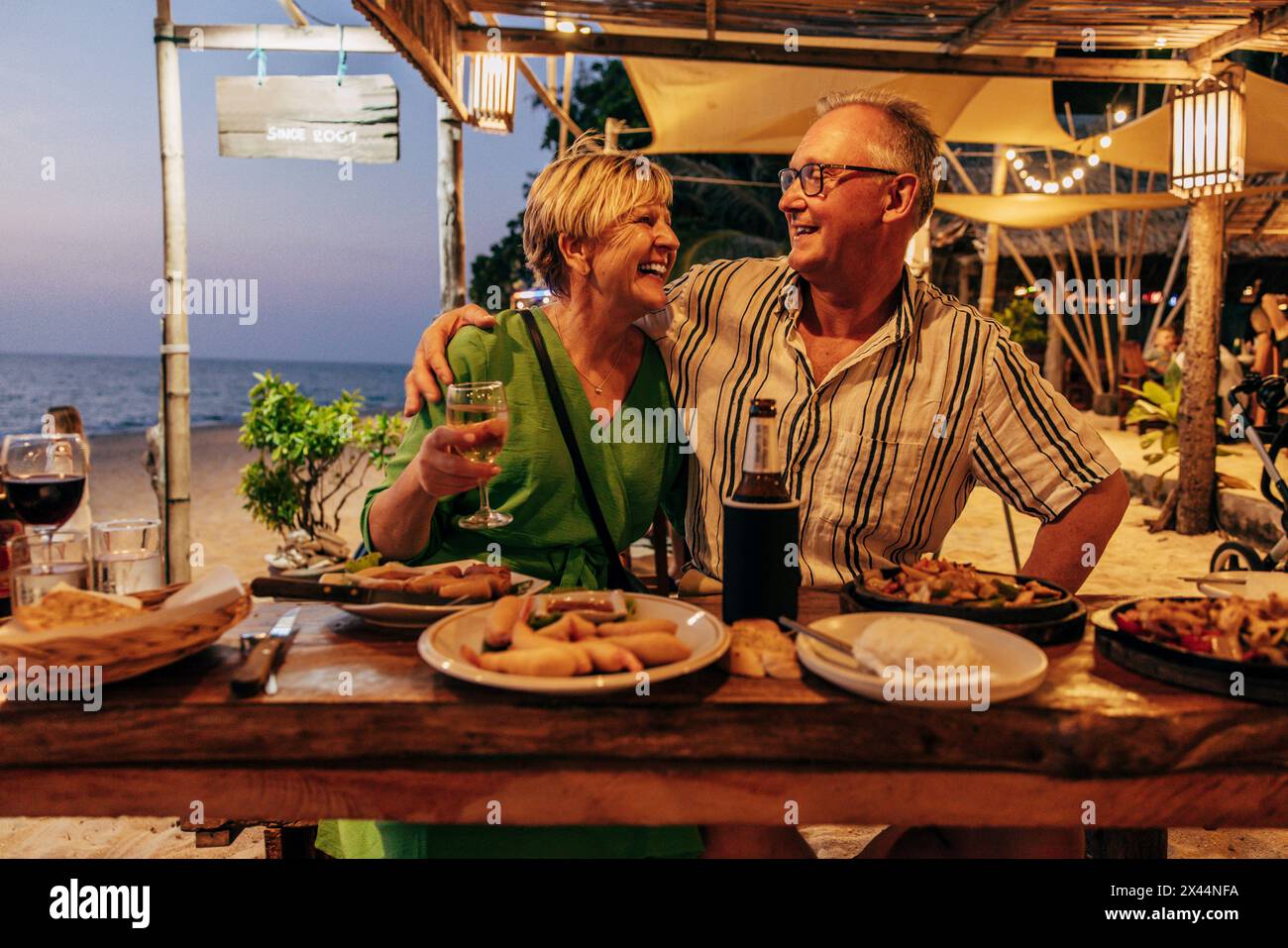 Glückliches Seniorenpaar, das Essen und Getränke genießt, während es im Strandrestaurant im Urlaub sitzt Stockfoto