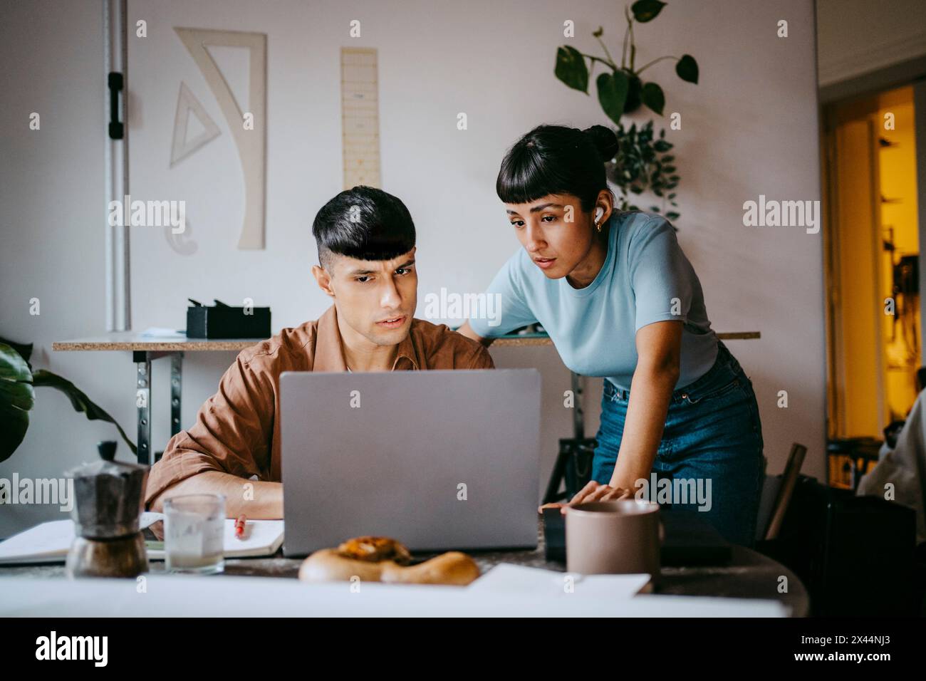Junger männlicher Freelancer erklärt weibliche Kollegin, während er im Home Office über Laptop spricht Stockfoto