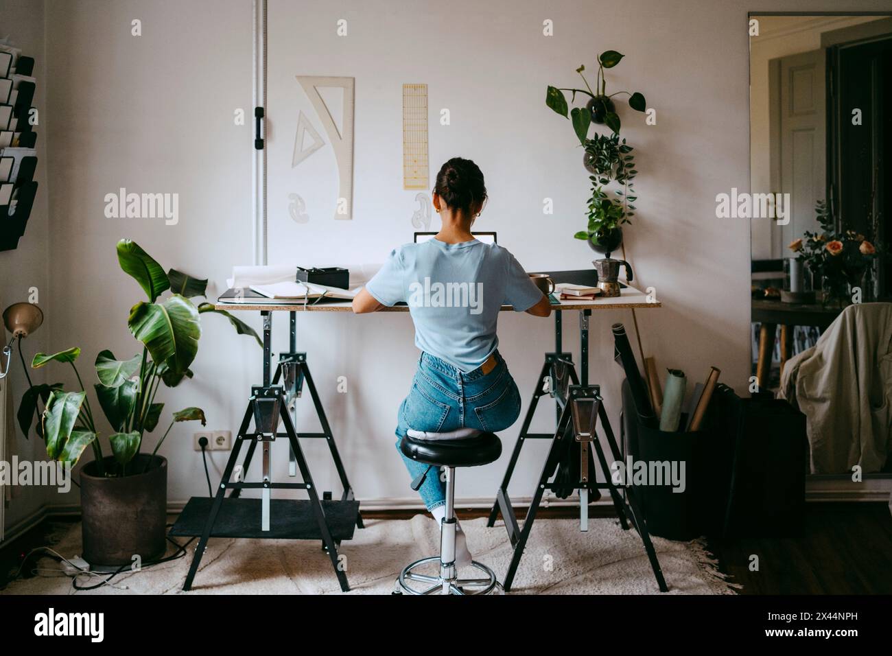 Rückansicht einer Freiberuflerin, die auf dem Hocker sitzt und von zu Hause aus arbeitet Stockfoto