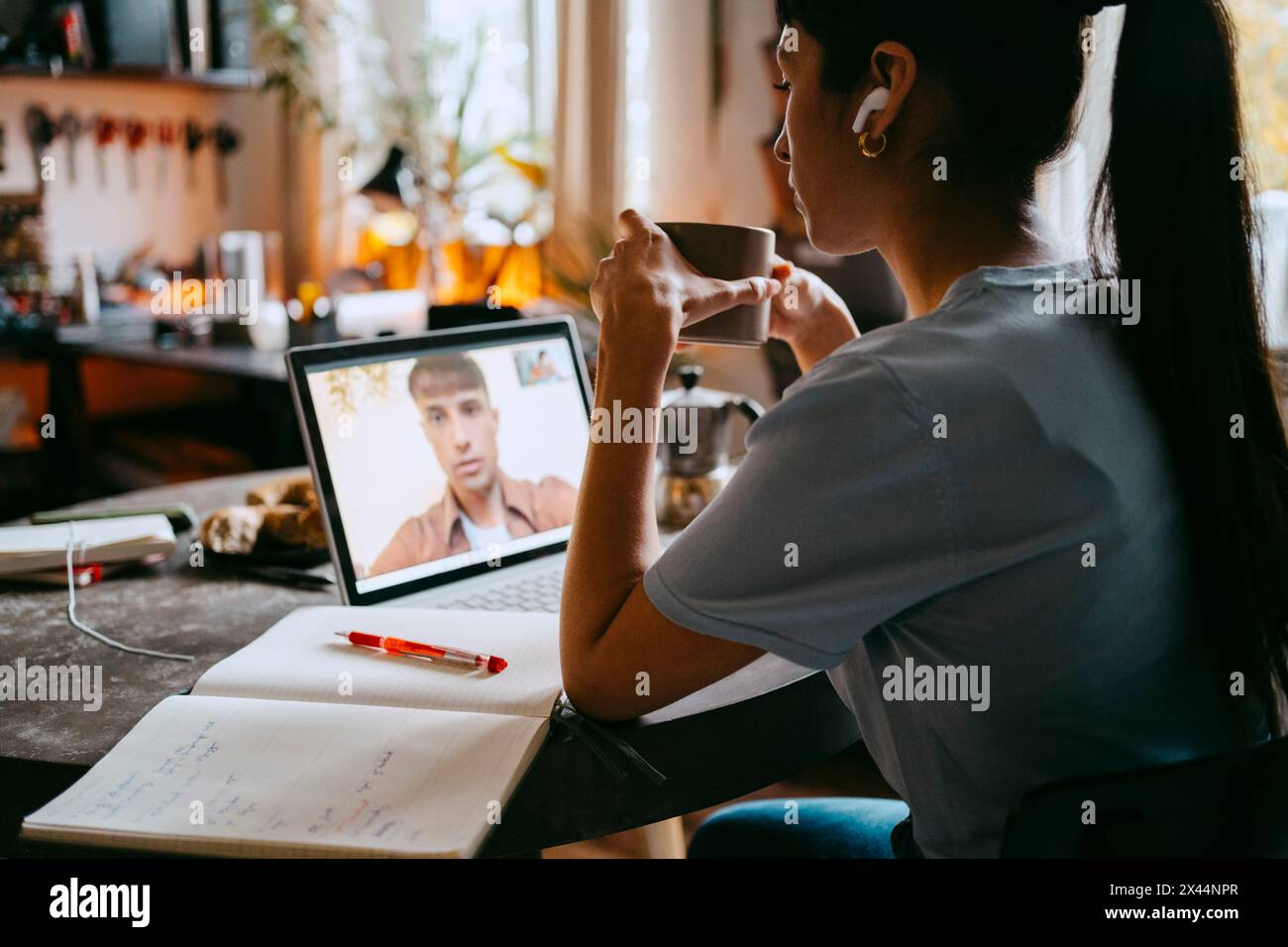 Junge Freiberuflerin, die eine Kaffeetasse hält, während sie im Heimbüro Videogespräche mit einem Kollegen auf einem Laptop führt Stockfoto