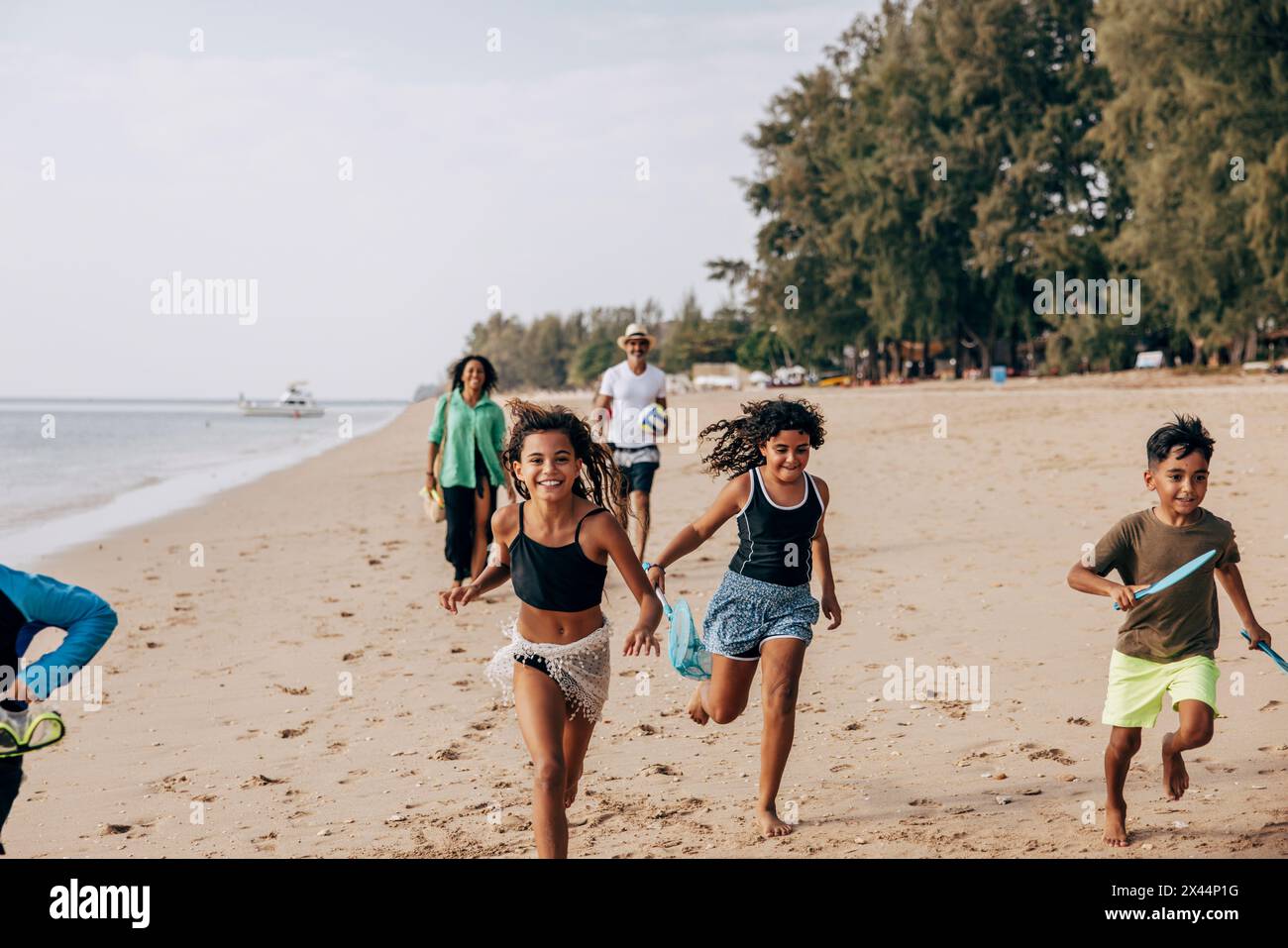 Fröhliche Kinder laufen auf Sand, Vater und Mutter laufen im Hintergrund am Strand Stockfoto