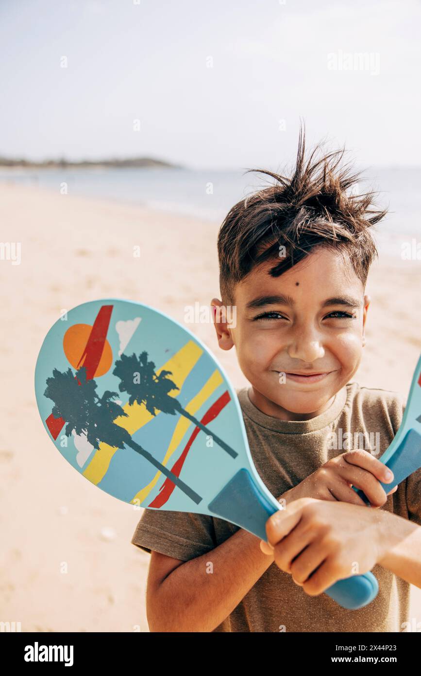 Porträt eines lächelnden Jungen mit gemusterten Schlägern am Strand Stockfoto