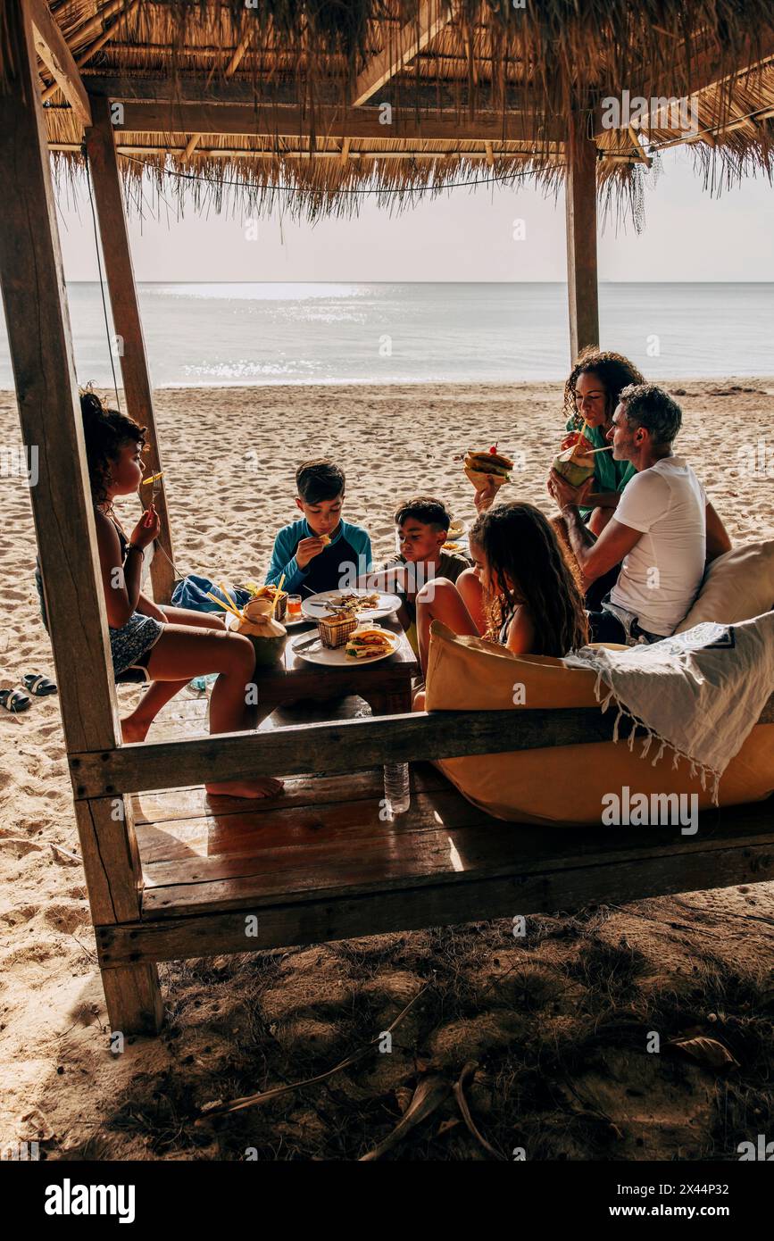 Familie genießt Abendessen, während sie im Urlaub zusammen in der Hütte am Strand sitzt Stockfoto