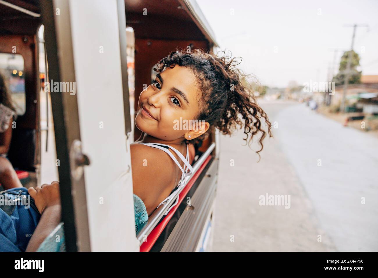 Lächelndes, sorgloses Mädchen, das sich aus dem Fenster lehnte, während er im Tuk-Tuk im Urlaub reiste Stockfoto