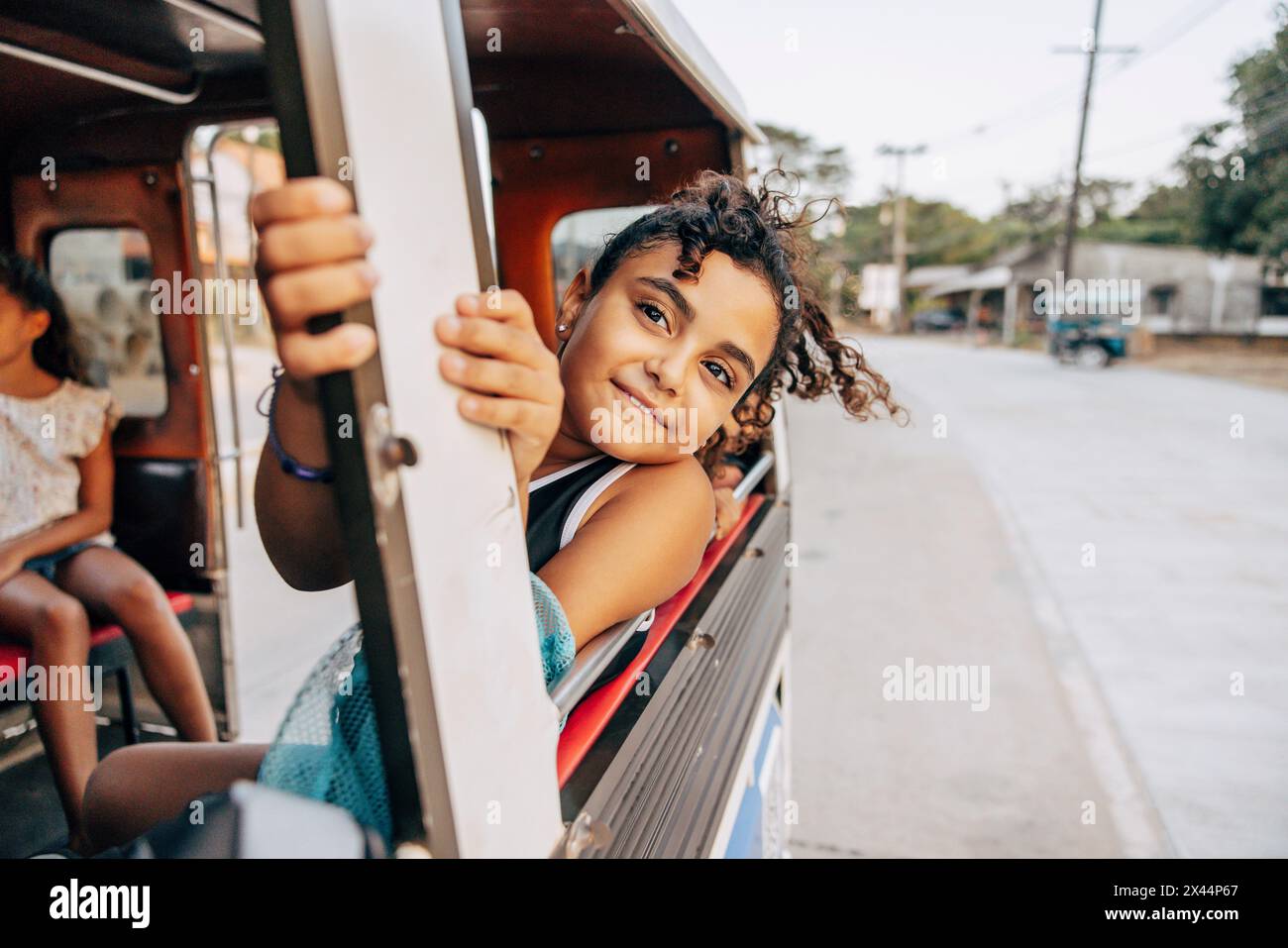 Lächelndes Mädchen, das sich während eines Roadtrips aus dem Fenster lehnte, während es im Tuk-Tuk im Urlaub saß Stockfoto