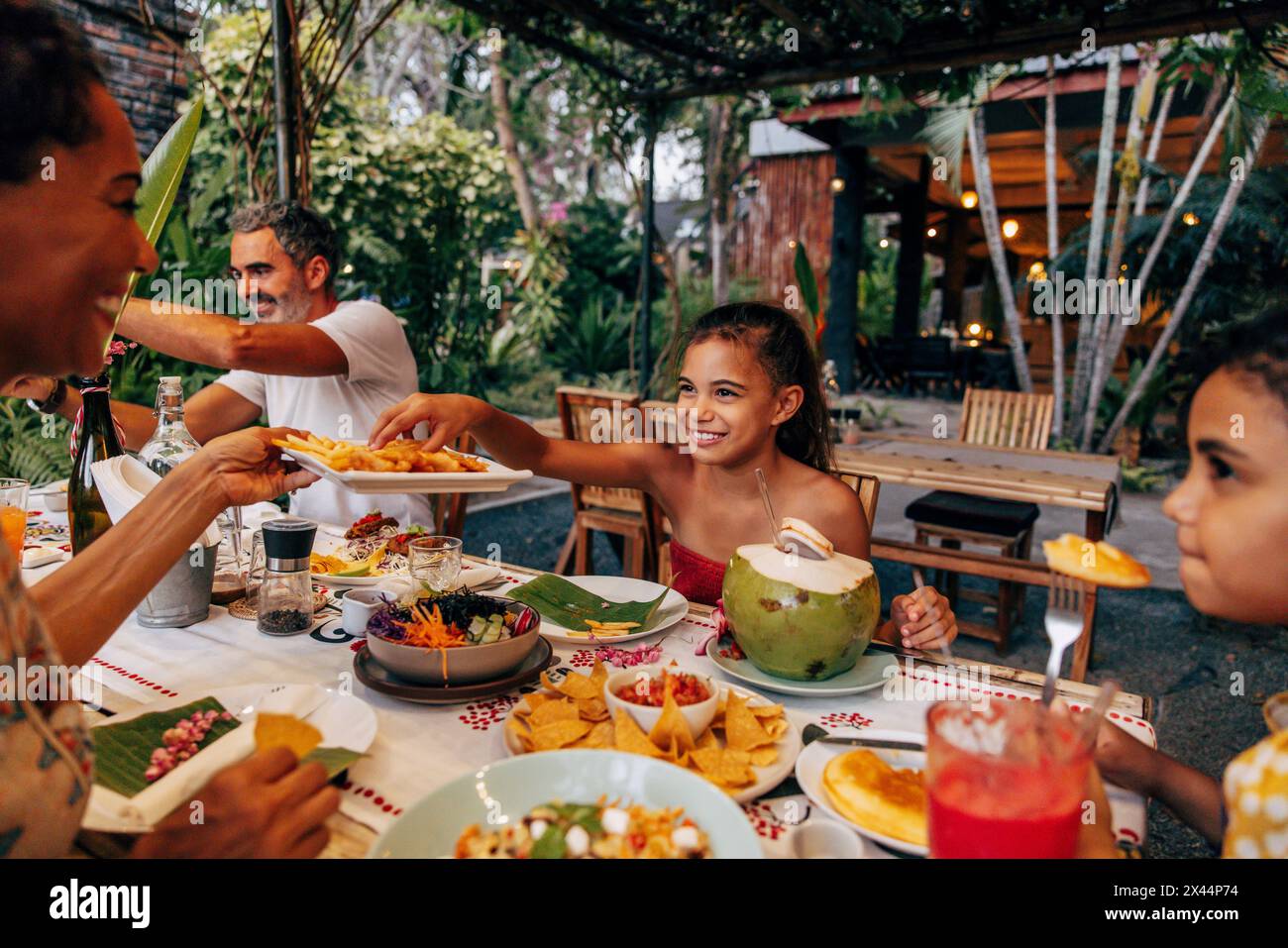 Lächelndes Mädchen, das Pommes vom Teller holte, während es mit der Familie im Resort im Urlaub zu essen war Stockfoto