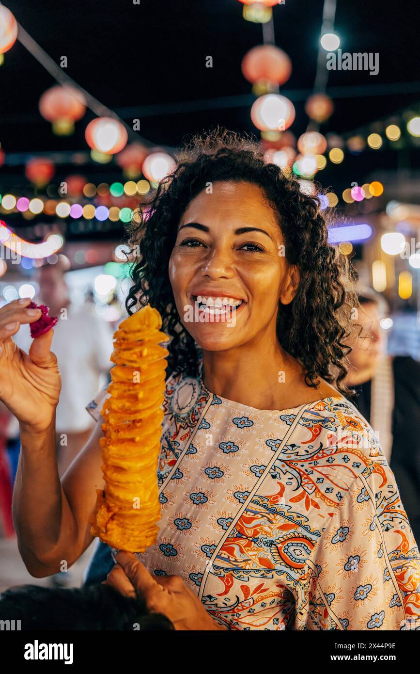 Porträt einer glücklichen Frau, die Tornadokartoffeln auf dem Lebensmittelmarkt im Urlaub hält Stockfoto