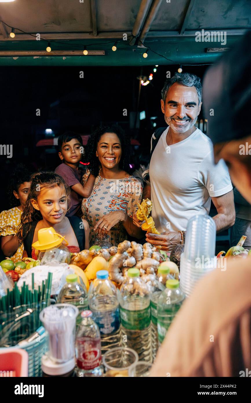 Lächelnde Familie, die mit dem Verkäufer am Saftstand auf dem Lebensmittelmarkt spricht Stockfoto