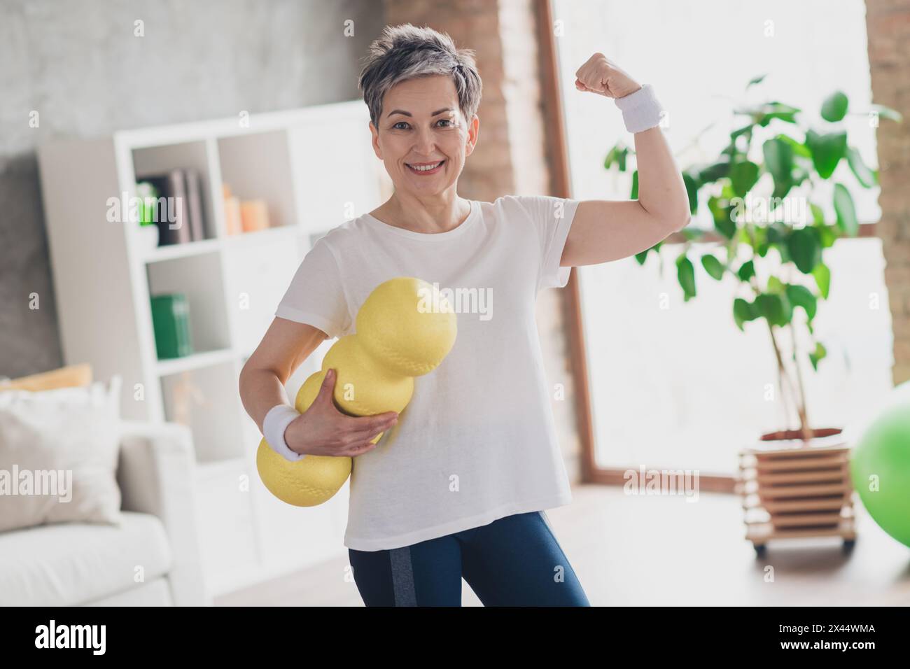 Foto einer attraktiven Seniorin halten Massage Roll Show Muskeln Sportswear Home Workout geräumiges helles Wohnzimmer Sportkonzept Stockfoto
