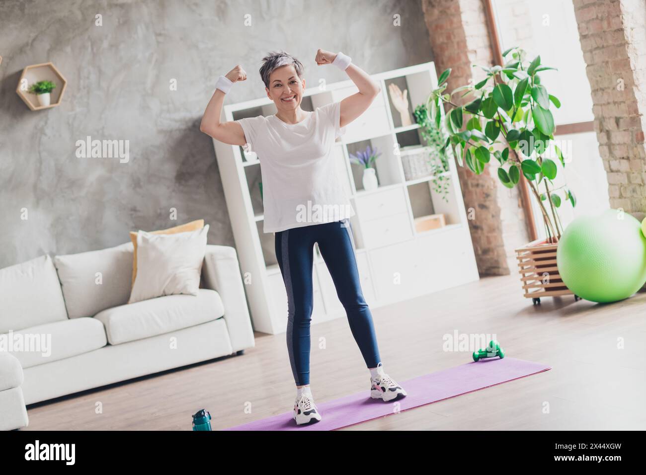 Foto in voller Länge von netten Rentner Frau zeigen Muskeln Sportswear nach Hause Training Routine Wohnzimmer gesunde Lebensweise Stockfoto