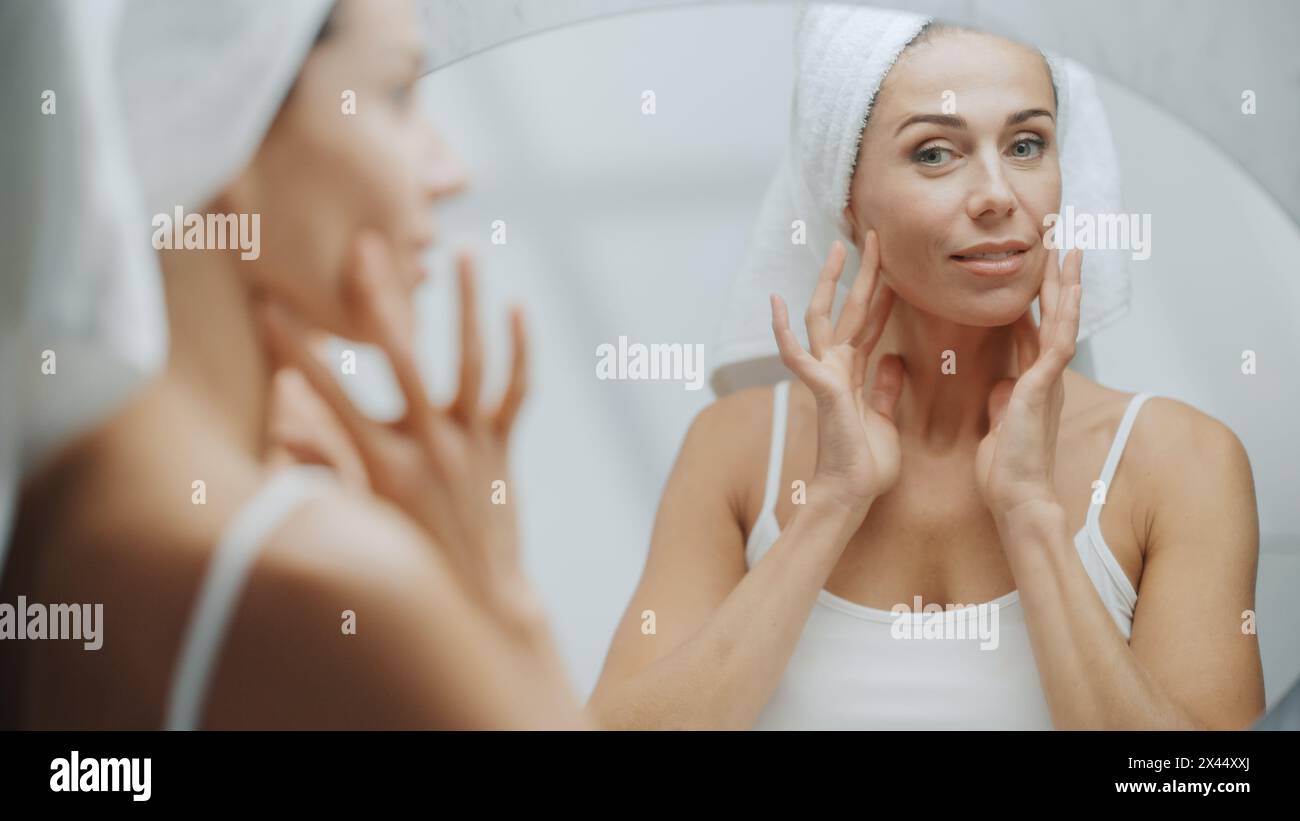 Schöne weiße Frau berührt ihre perfekte weiche Schulter, Hals, sinnlich sieht im Badezimmerspiegel aus. Frau Mittleren Alters Genießt Ihre Natürliche Schönheit Morning Routine. Überschulteraufnahme Stockfoto