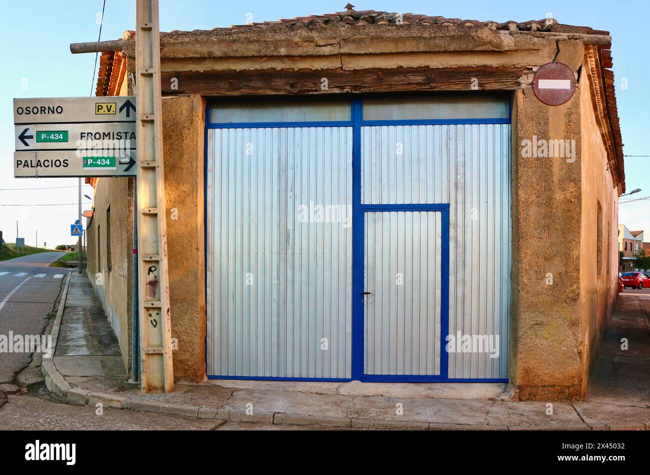 Alte Scheune mit neuen Metalltüren an einer Ecke an einer Kreuzung mit Straßenschildern im Abendlicht Lantadilla Palencia Castile und Leon Spain Stockfoto