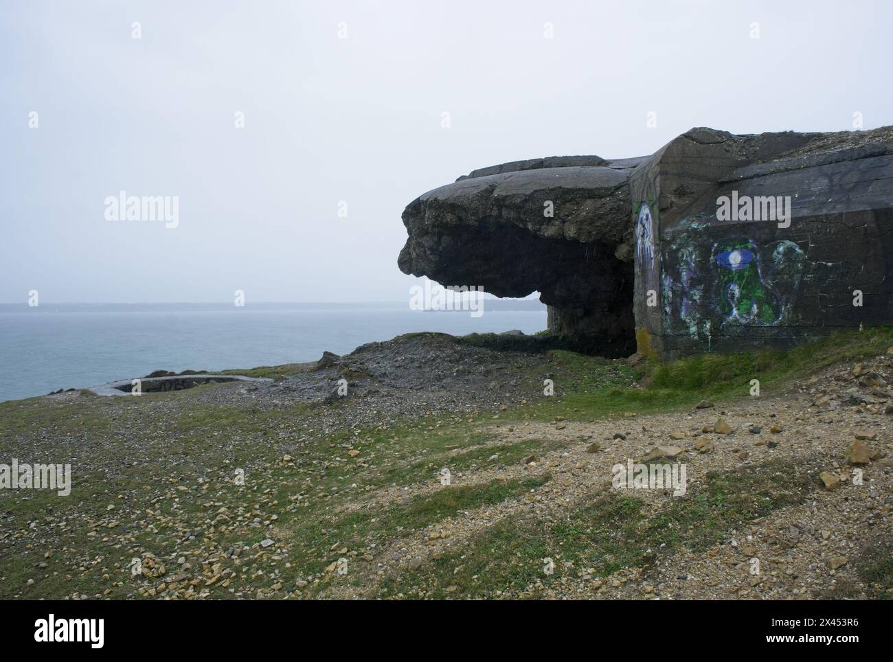 Blick auf die Küste von außen auf einen bombardierten deutschen Bunker aus dem Zweiten Weltkrieg auf dem Anse de Pen hat, Bretagne. Leuchtturm. Bewölkter Frühlingstag. Selektiver Fokus Stockfoto