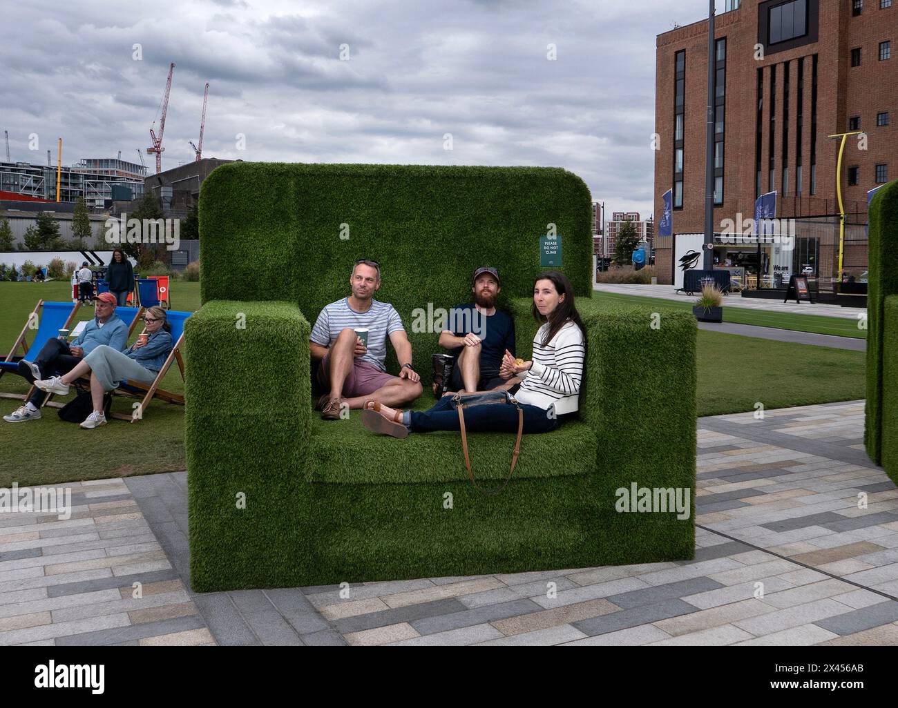 Drei Leute sitzen in einem überdimensionalen Stuhl mit Gras vor dem Battersea-Kraftwerk Stockfoto