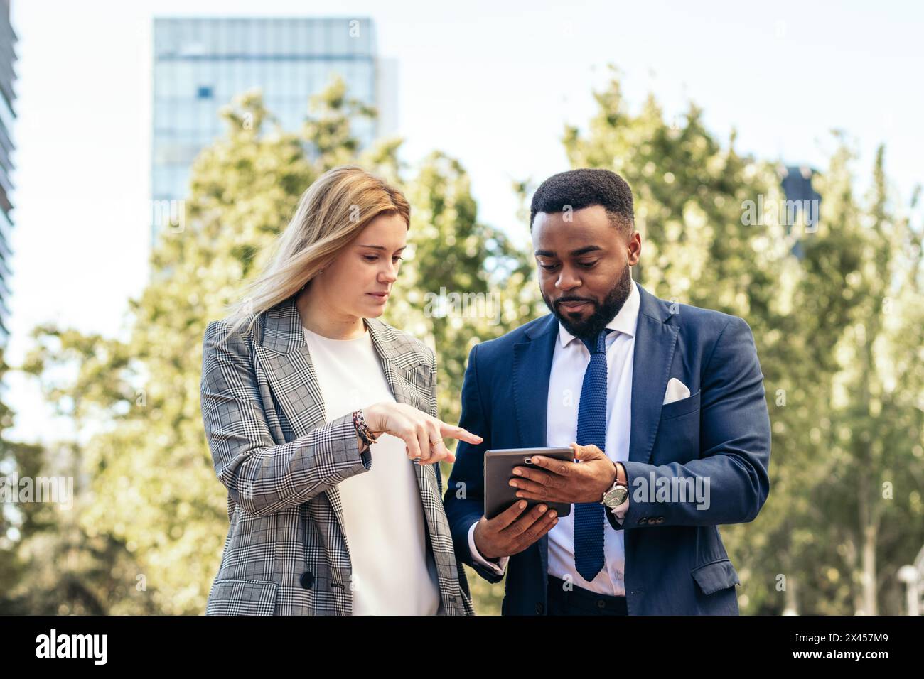 Geschäftsleute in Bürokleidung, die ein Tablet verwenden, um außerhalb des Büros über Unternehmensdaten zu sprechen Stockfoto