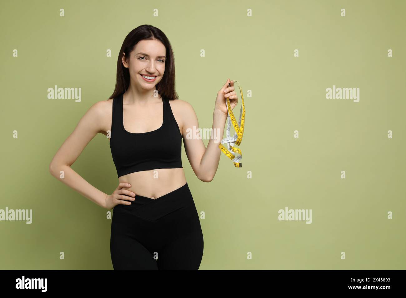 Glückliche junge Frau mit Maßband, die ihren schlanken Körper auf grünem Hintergrund zeigt, Platz für Text Stockfoto