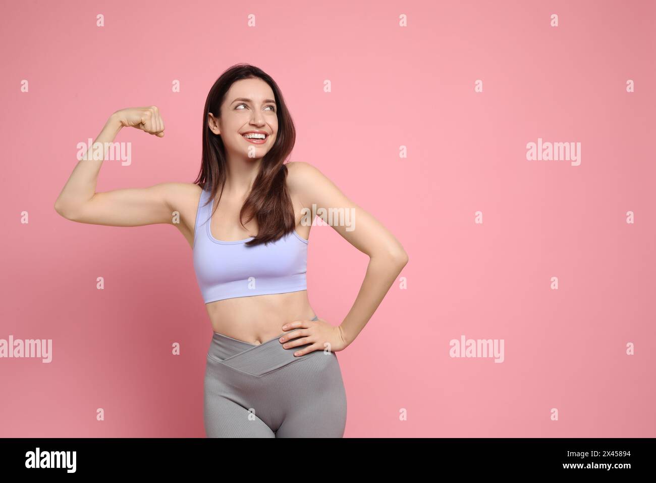 Glückliche junge Frau mit schlankem Körper, die ihre Muskeln auf rosa Hintergrund zeigt, Platz für Text Stockfoto