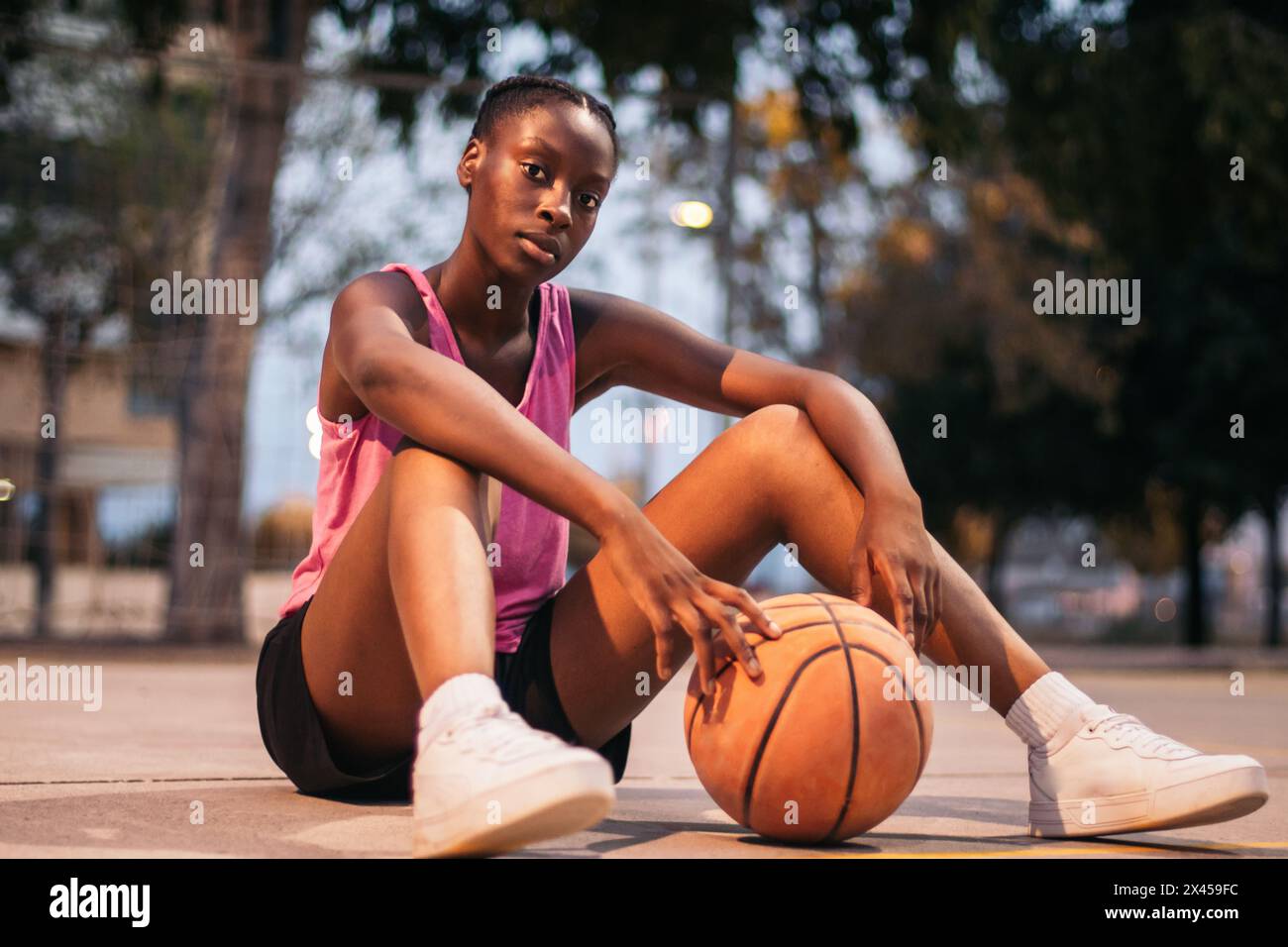 Sportliche schwarze Frau, die mit Basketball auf dem Basketballfeld sitzt Stockfoto