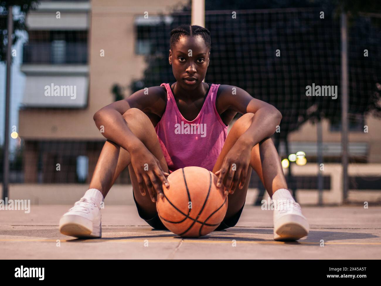Sportliche schwarze Frau, die mit Basketball auf dem Basketballfeld sitzt Stockfoto