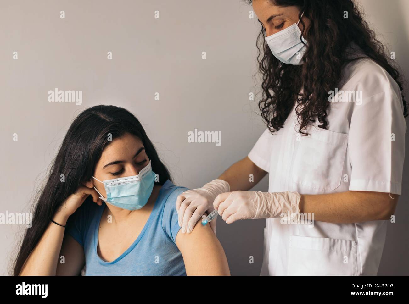 Arzt macht Impfung für junge Frau mit chirurgischer Maske Stockfoto