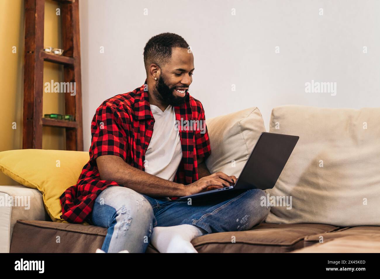 Lächelnder schwarzer Mann, der von zu Hause aus mit einem Laptop arbeitet. Telearbeit und Home Office-Konzept. Stockfoto