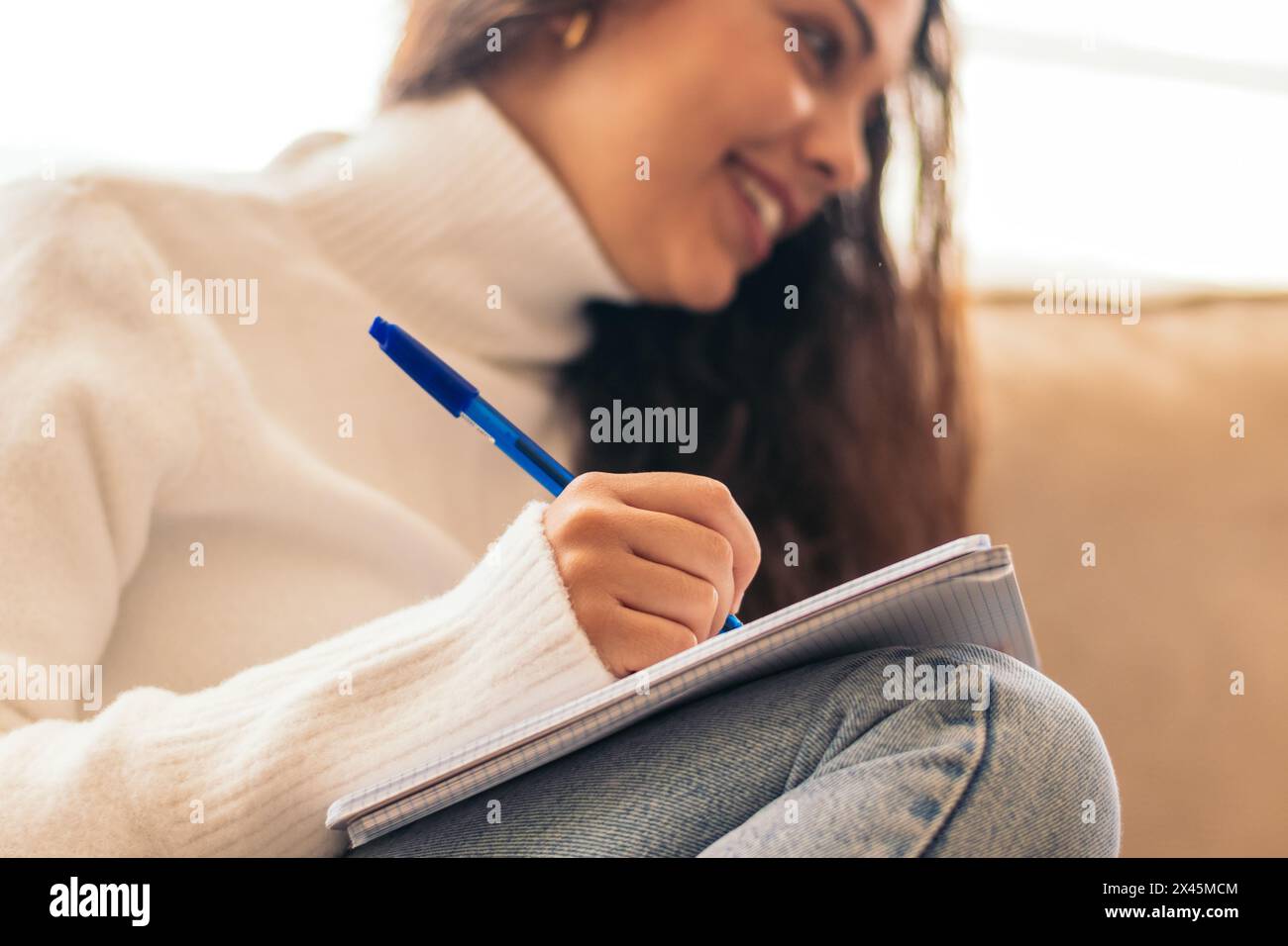 Eine junge Frau, die zu Hause sitzt und mit ihrem Laptop und einem Notizbuch für die Universität studiert. Der Teilnehmer macht sich Notizen, während er sich die Informationen online ansieht Stockfoto