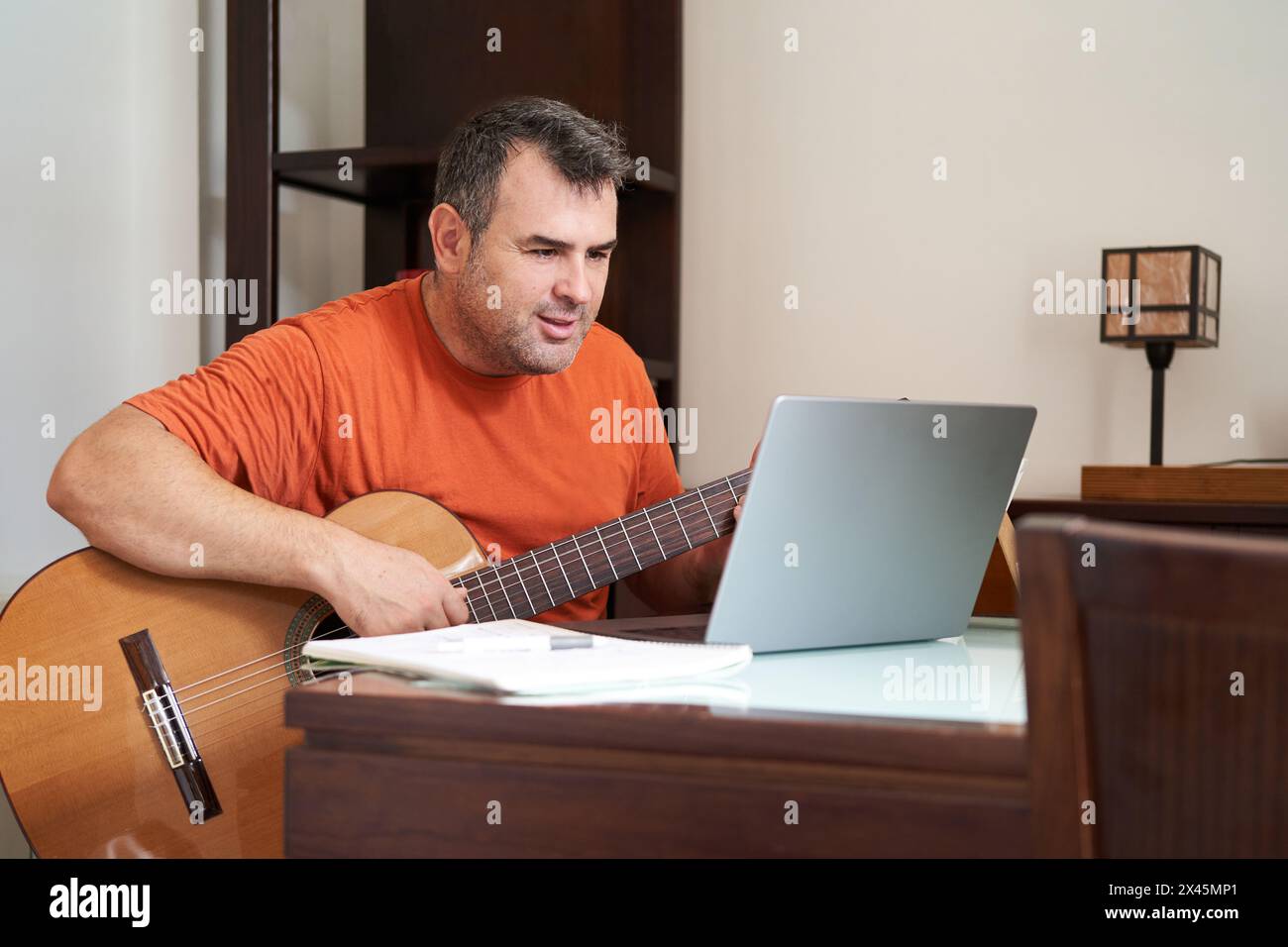 Ein Mann mit Laptop im Online-Gitarrenunterricht, der Harmonien lernt Stockfoto