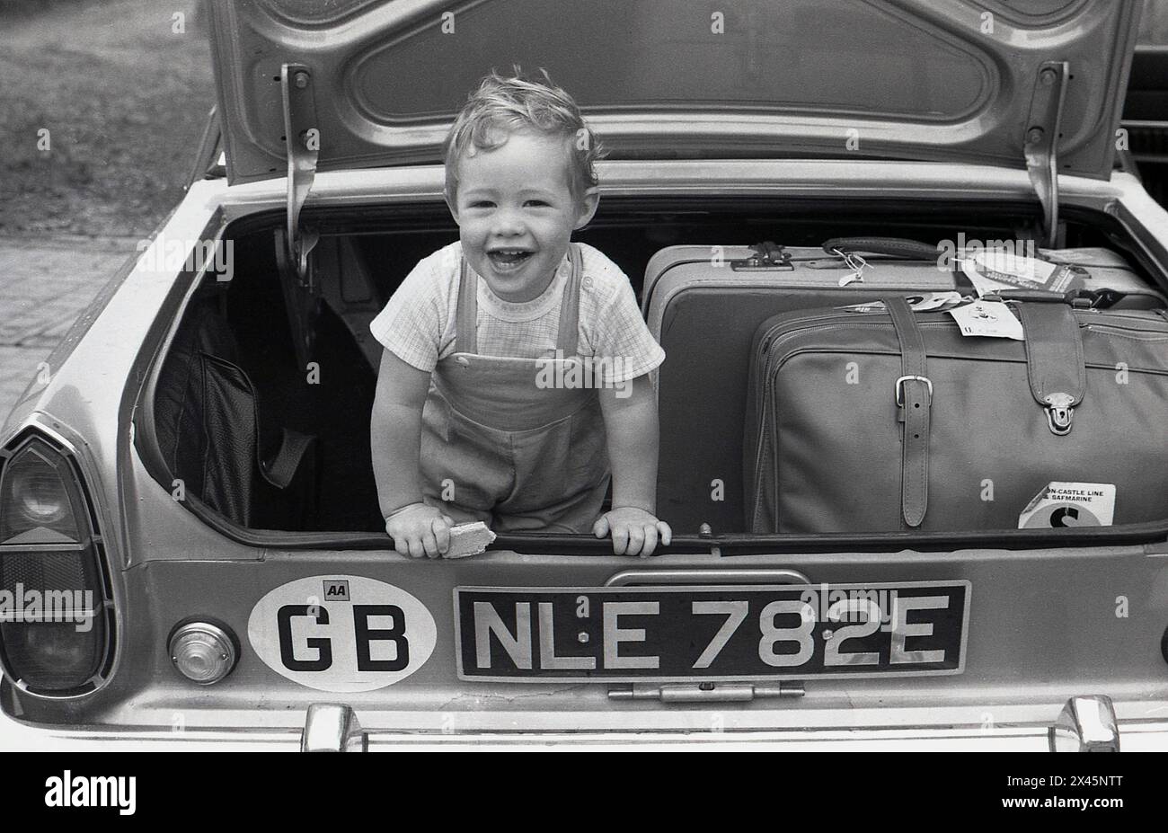 1960er Jahre, historisch, ein kleiner Junge, der einen Wafer hält, mit Gepäck im offenen Kofferraum eines Autos der Epoche, eines Ford Corsair. Auf den Koffern Gepäcketiketten mit Angabe der Union-Castle-Linie/Safmarine. Crusie Shpips, betrieben von der South Africa Marine Corporation, einer südafrikanischen Reederei mit Sitz in Kapstadt. Stockfoto