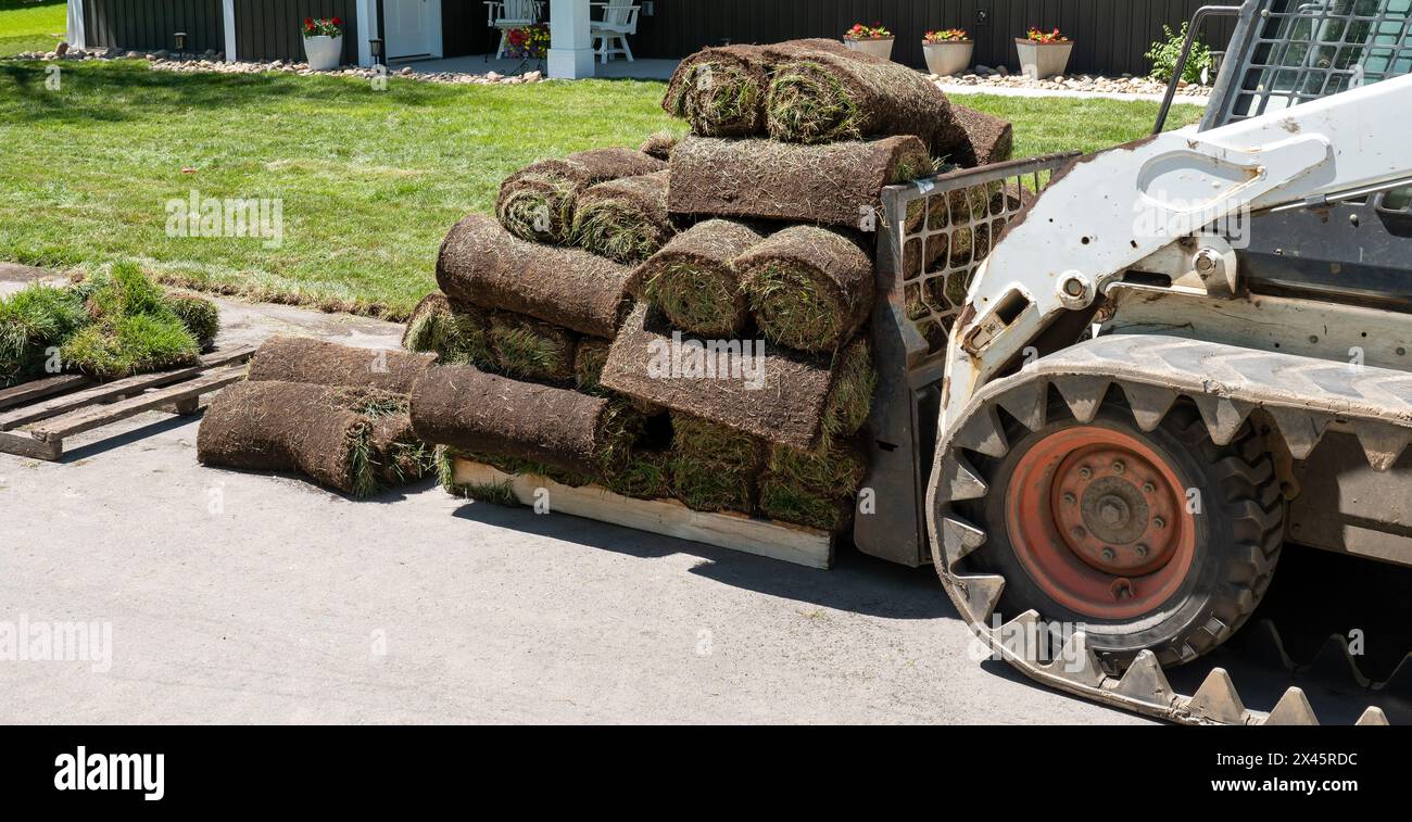 Ein kompakter Frontlader und eine Palette mit Rollen frischem Gras für den Einbau auf einer neuen Baustelle mit neu installiertem Gras Stockfoto