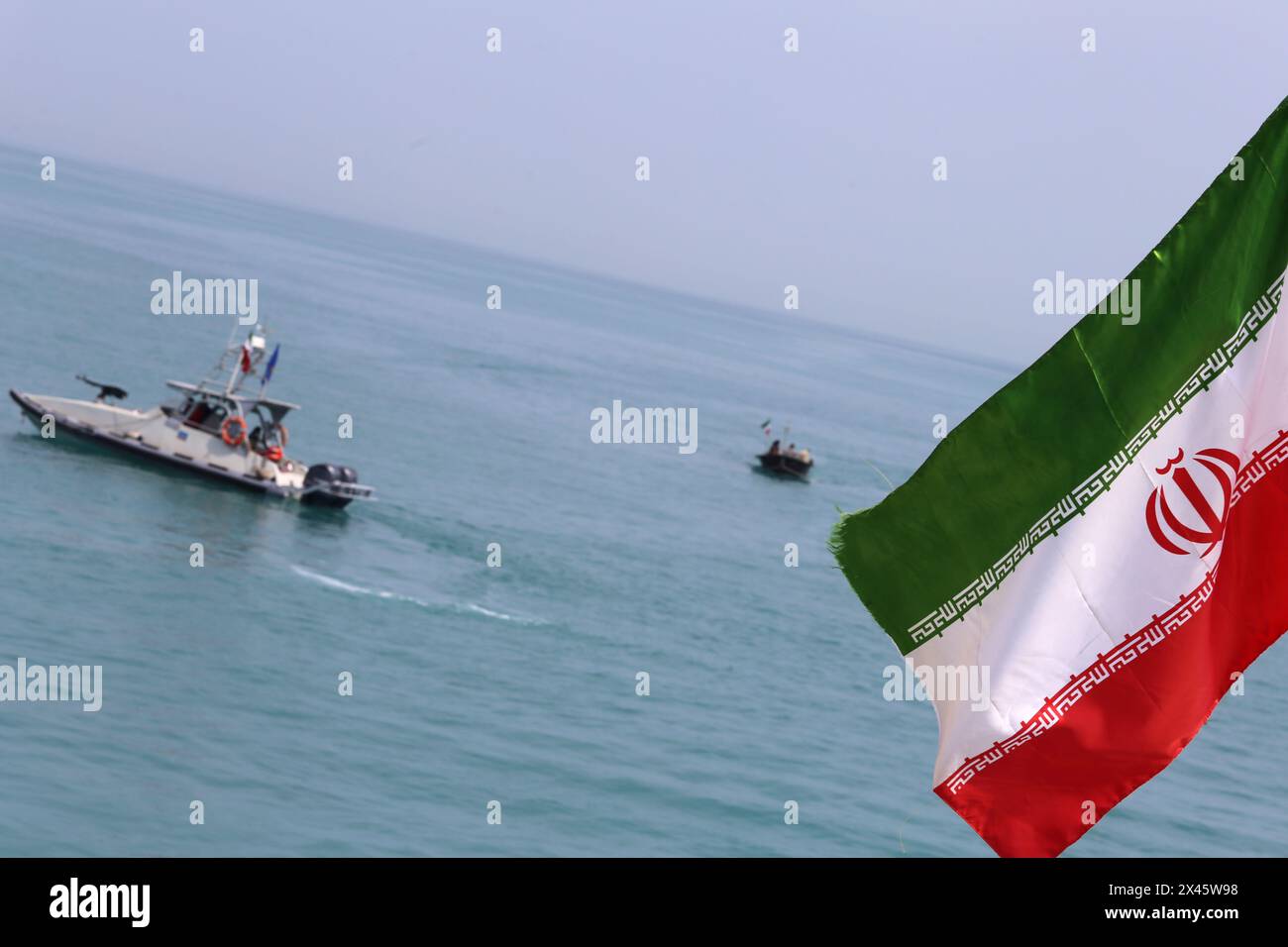 April 2024, Persischer Golf, Buschehr, Iran: die Schnellboote des Korps der Islamischen Revolutionsgarde (IRGC) segeln entlang des Persischen Golfs, während die iranische Flagge während der Marineparade der IRGC zum Nationalfeiertag des Persischen Golfs in der Nähe des Kernkraftwerks Bushehr in der Hafenstadt Bushehr in der Provinz Bushehr im Süden des Iran winkt. Der Iran feiert den Jahrestag der Befreiung des Südens des Landes von der portugiesischen Besatzung im Jahr 1622 als „Nationalfeiertag am Persischen Golf“ am 29. April 2024 in Buschehr. Das Datum fällt mit dem Jahrestag eines erfolgreichen Militärkampfes von Shah Abbas zusammen. Stockfoto