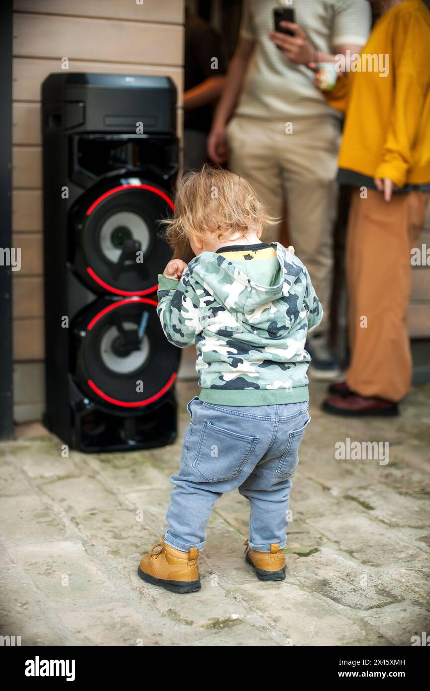 Ein entzückendes, fröhliches Kleinkind tanzt und bewegt sich zum Beat neben einem riesigen Soundlautsprecher auf dem Bürgersteig der Stadt. Straßenparty. Urbanes Leben Stockfoto