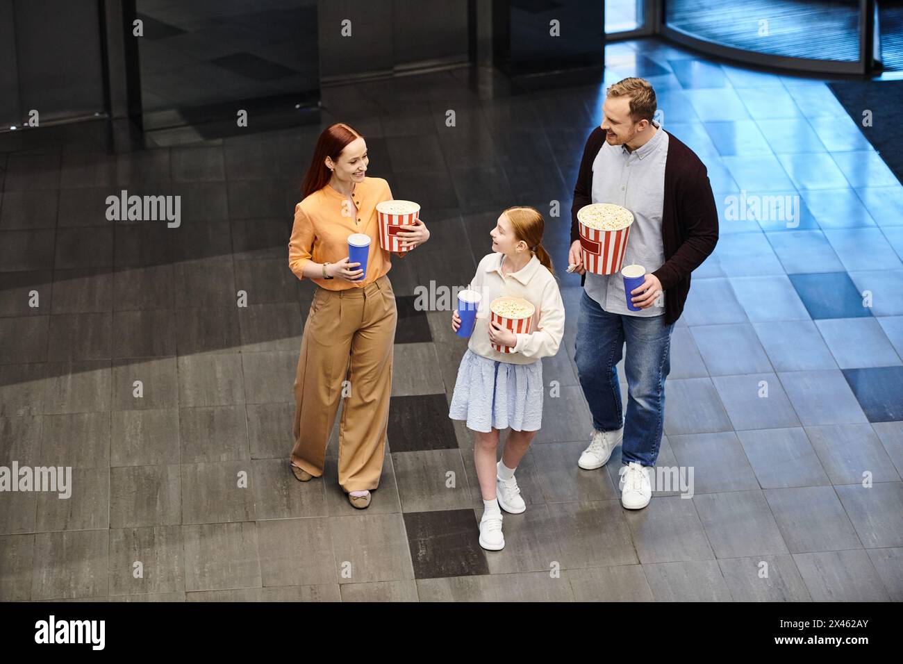 Vater und Sohn halten Popcorn, während ein kleines Mädchen neben ihnen im Kino steht und einen glücklichen Familienmoment genießt. Stockfoto