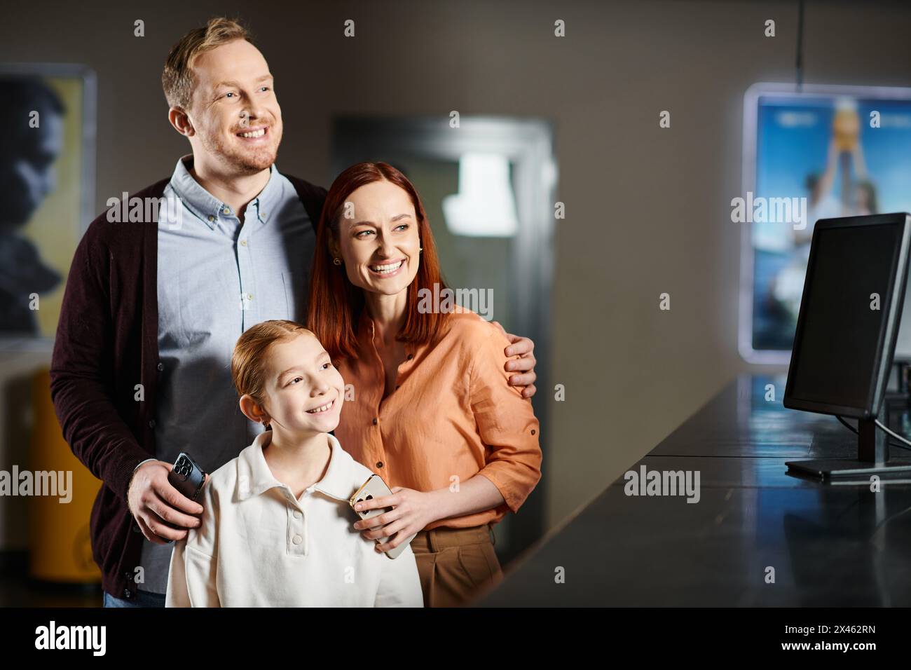 Ein Mann und eine Frau stehen neben einem Jungen im Kino und genießen gemeinsam einen Film als glückliche Familie. Stockfoto