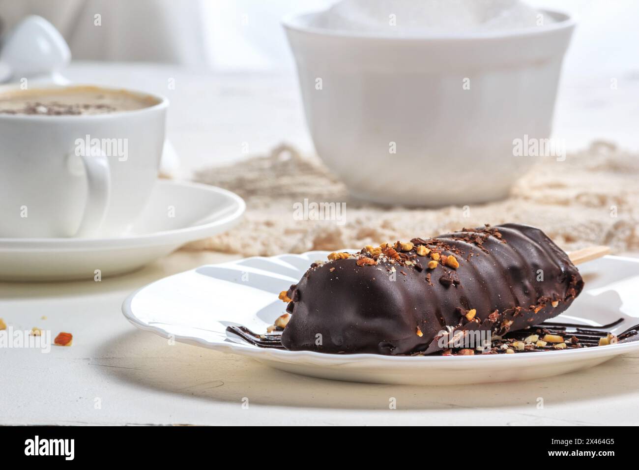 Essen, Stille, Leben im Stil eines hohen Schlüssels. Schokoladenkuchen mit Nüssen in Form von Eis am Stiel auf dem Teller und einer Tasse heißem сappuccino-Kaffee o Stockfoto