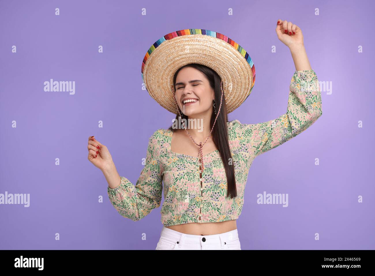 Junge Frau mit mexikanischem Sombrero-Hut, der auf violettem Hintergrund tanzt Stockfoto