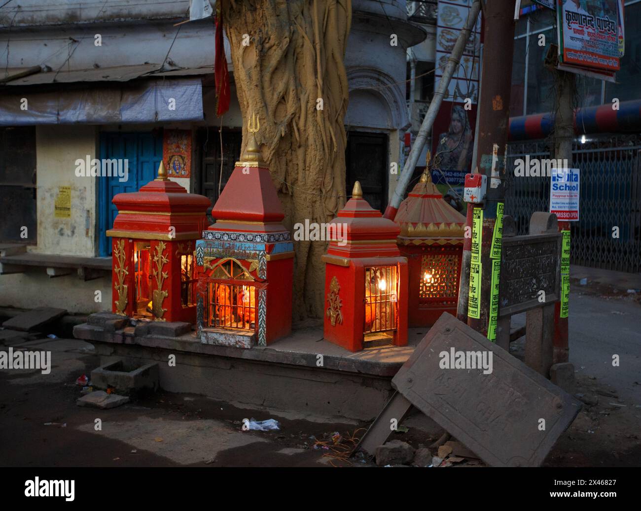 Vier kleine Schreine mit Beleuchtung neben einem großen Baumstamm am Straßenrand in Varanasi, Indien. Stockfoto