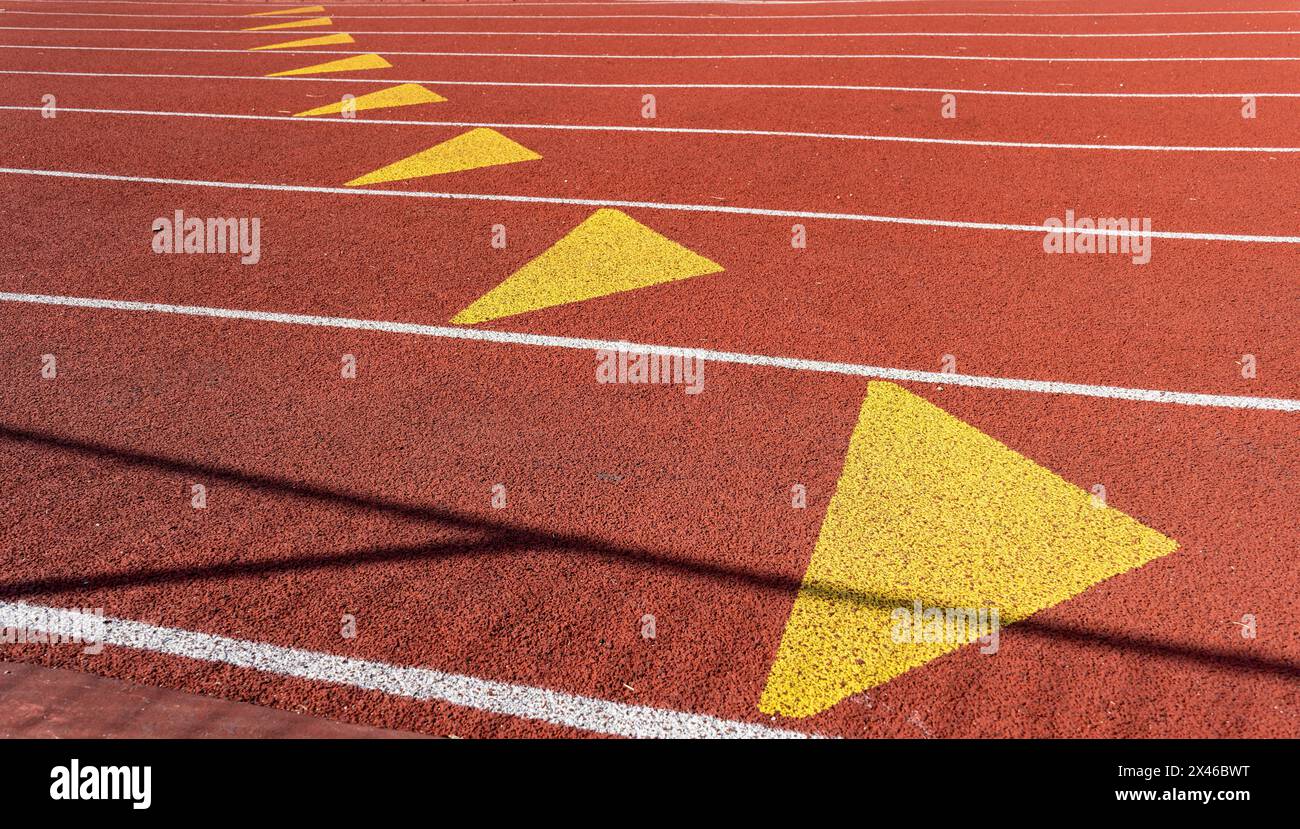 Nahaufnahme einer roten Leichtathletikbahn mit weißer Spurmarkierung, gelben Dreiecken und granularer Textur in einem Outdoor-Sportzentrum in Paris Stockfoto