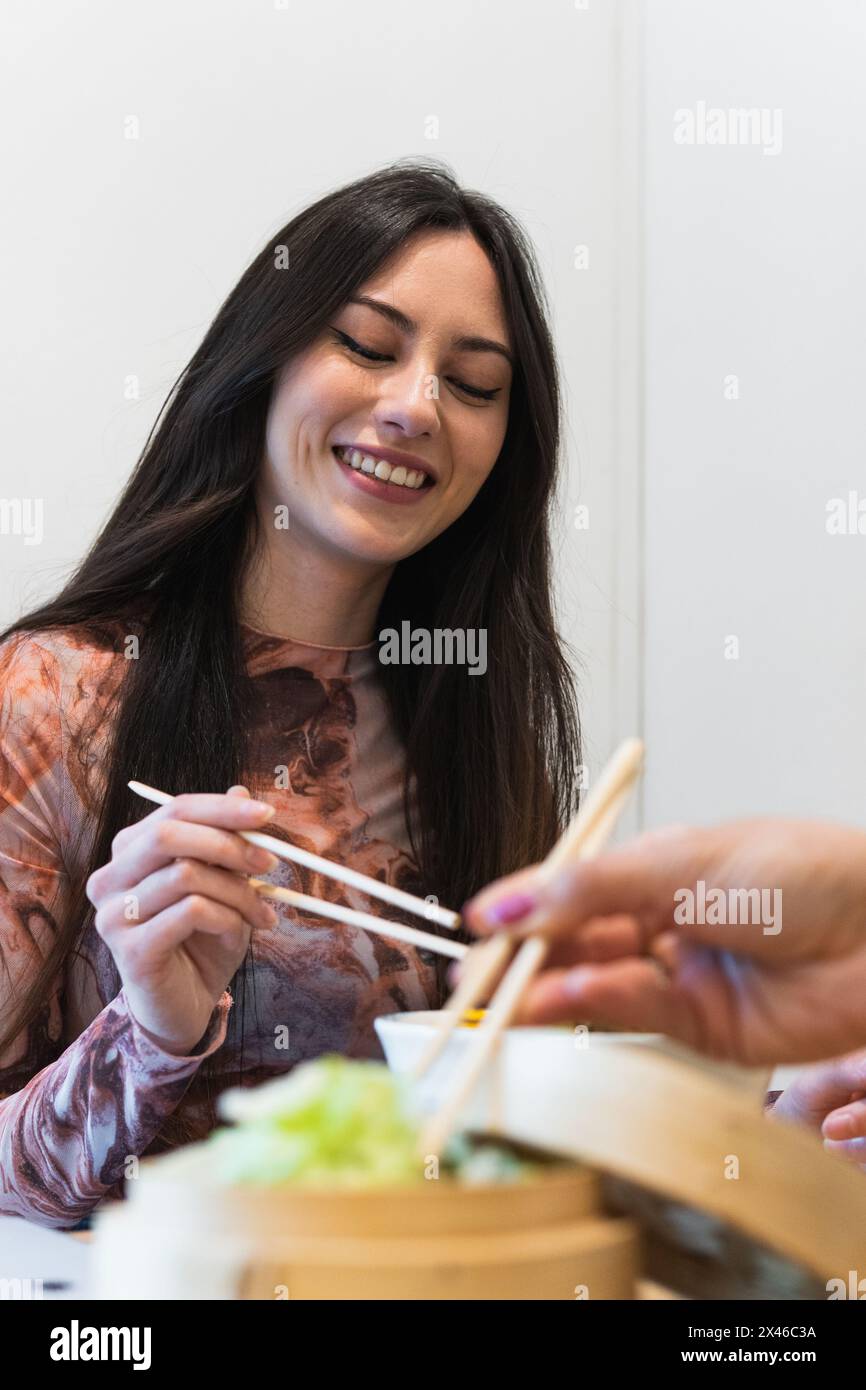 Frau, die am Tisch sitzt und mit einem anonymen Freund isst, der ein leckeres Sack isst, während er ein Wochenende im Restaurant verbringt Stockfoto