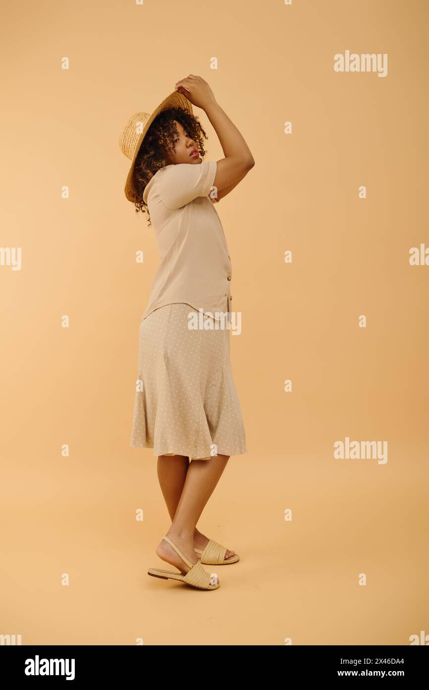 Eine schöne junge Afroamerikanerin mit lockigem Haar, ein weißes Kleid und Strohhut in einem Studio-Setting. Stockfoto