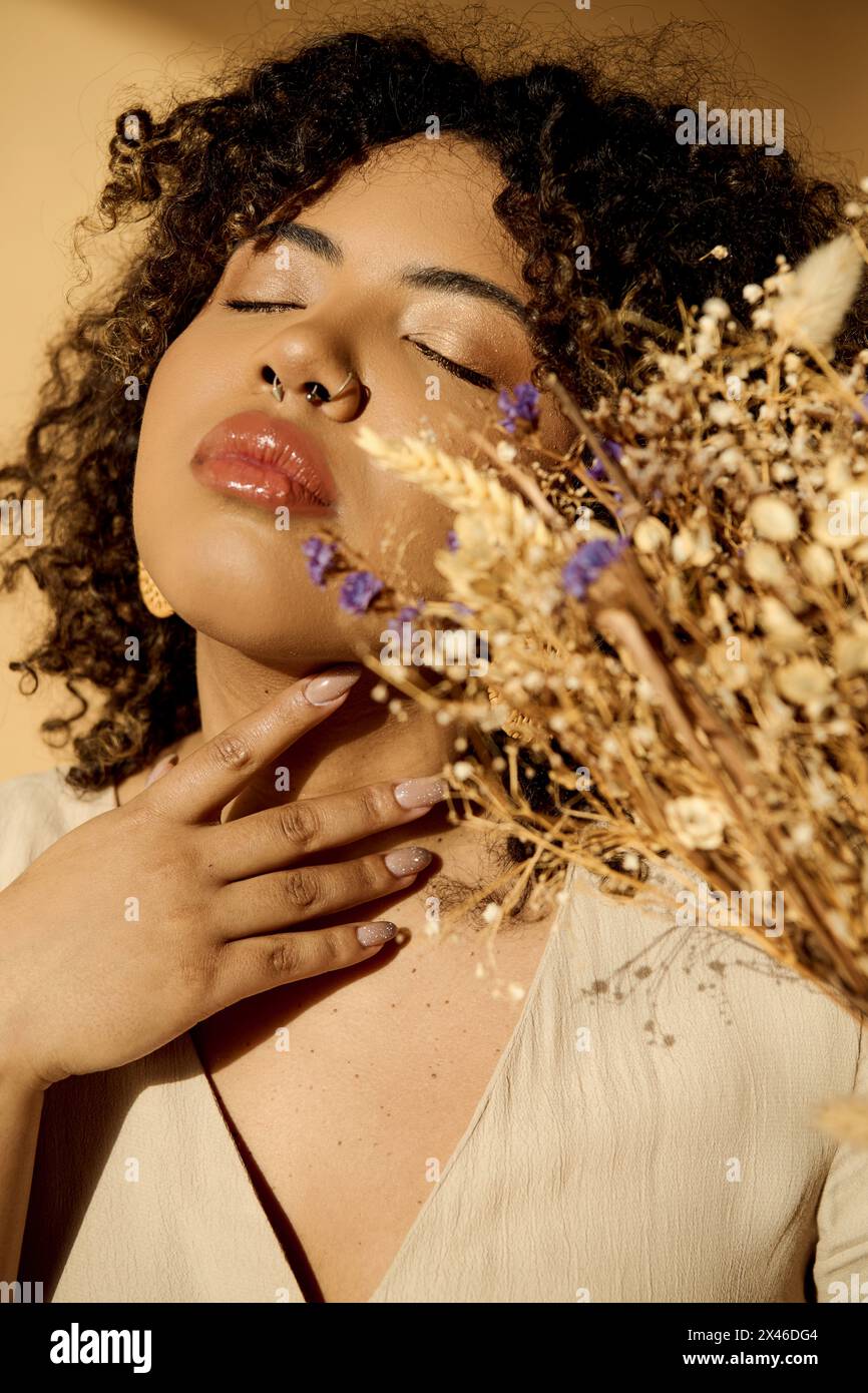 Eine schöne junge Afroamerikanerin in einem Sommerkleid, die einen Haufen getrockneter Blumen mit lockigen Haaren in einem Studio hält. Stockfoto