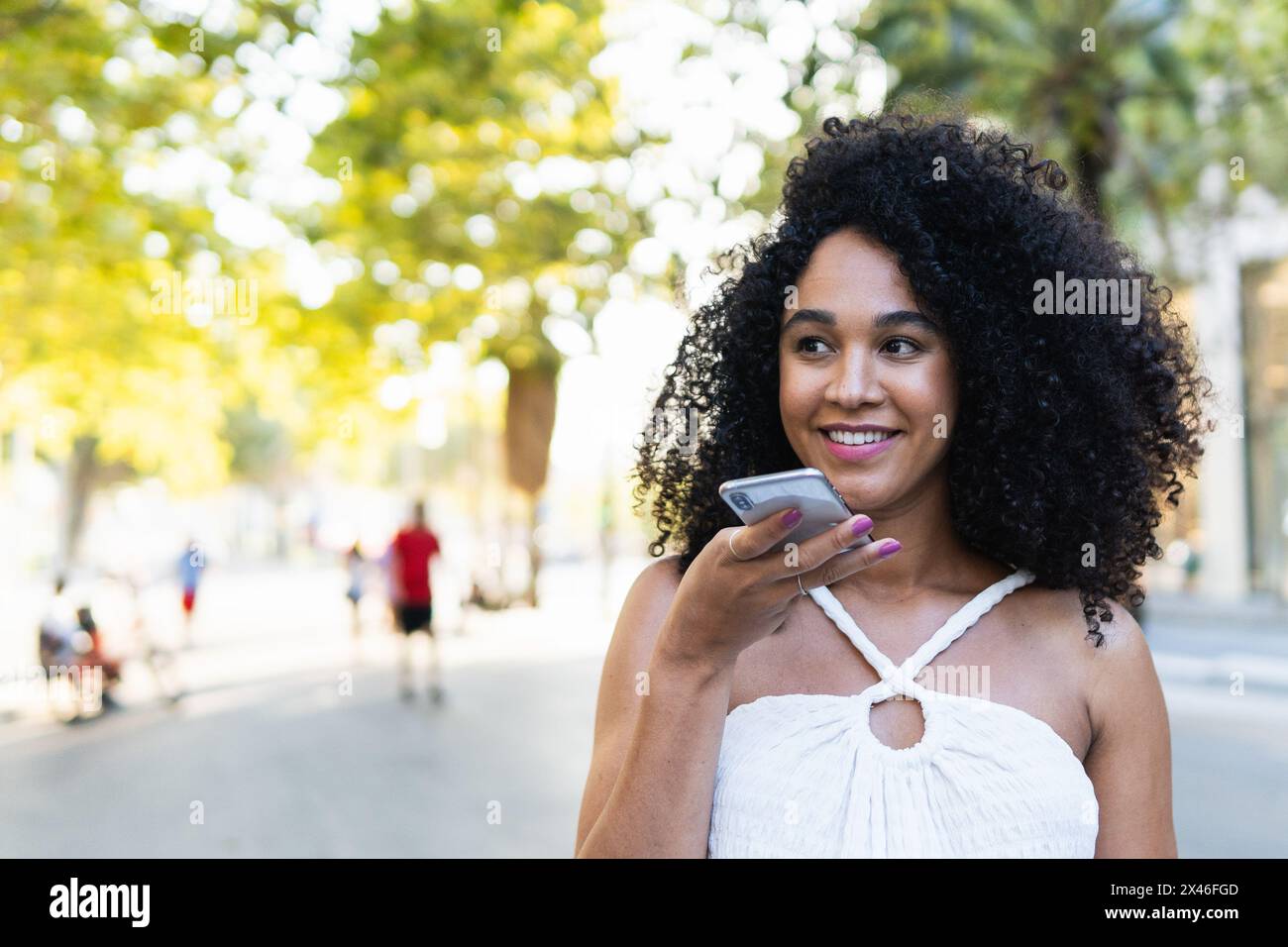 Positive afroamerikanische Frau mit Afro-Frisur, die Sprachnachrichten auf dem Handy auf der Straße der Stadt aufzeichnete Stockfoto