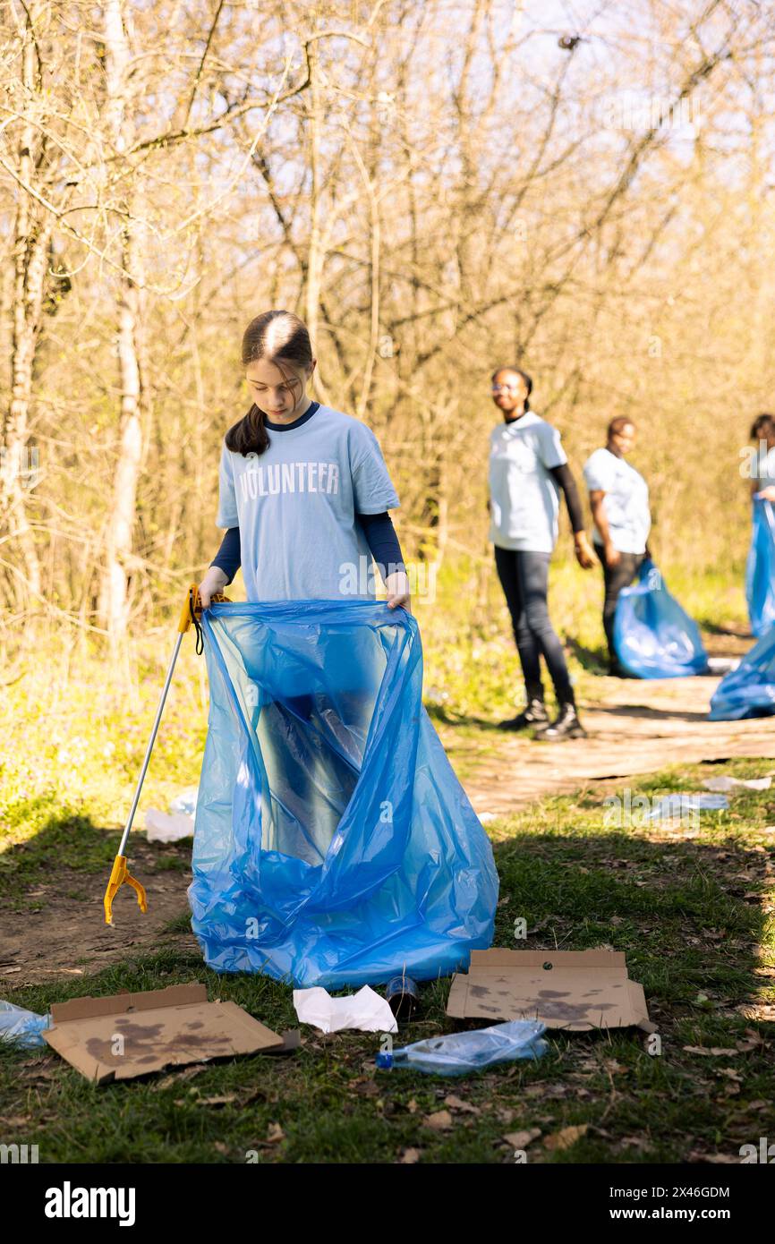 Der Freiwillige des Gemeindedienstes reduziert Abfall und reinigt Waldflächen, indem er Müll in blauen Müllsäcken sammelt. Junge Kinder tragen zur Erhaltung der Umwelt bei, indem sie Kunststoffabfälle entsorgen. Stockfoto
