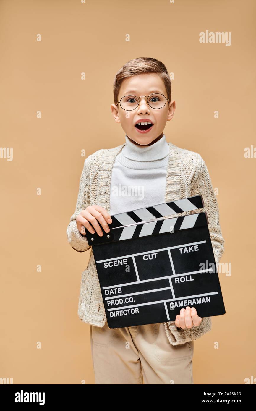 Ein kleiner Junge, der als Filmregisseur verkleidet ist, hält eine Klatschtafel vor seinem Gesicht. Stockfoto