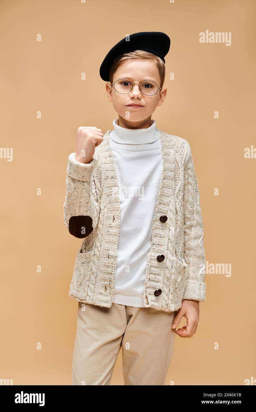 Ein kleiner Junge in einem Pullover mit Brille, träumt und kreiert vor beigefarbenem Hintergrund. Stockfoto